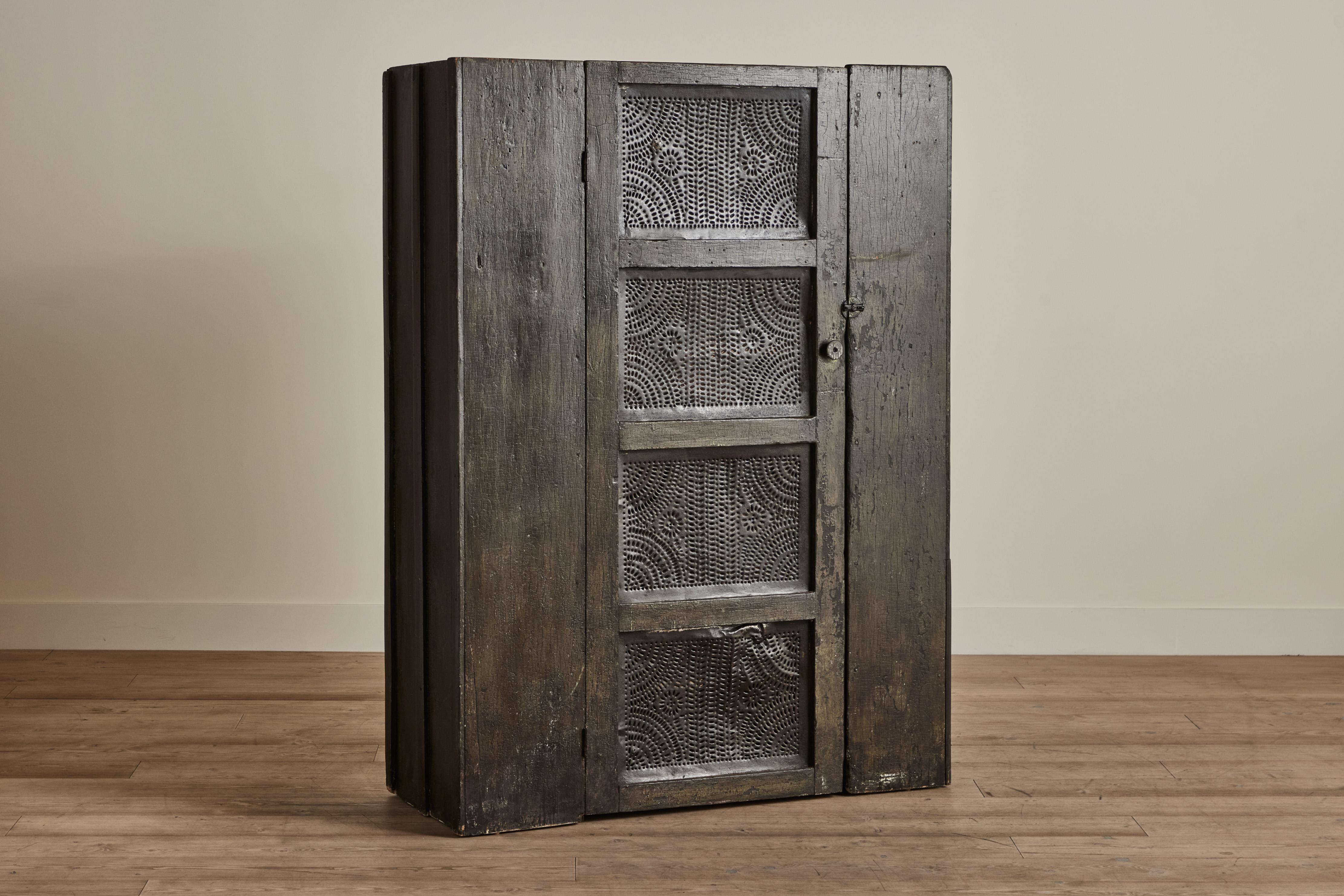 Large tin punch pie cabinet with a stunning blacked finish. The finish looks slightly dark green. This early American piece has interior shelving for ample storage. Heavy visible wear throughout that is consistent with age and use.