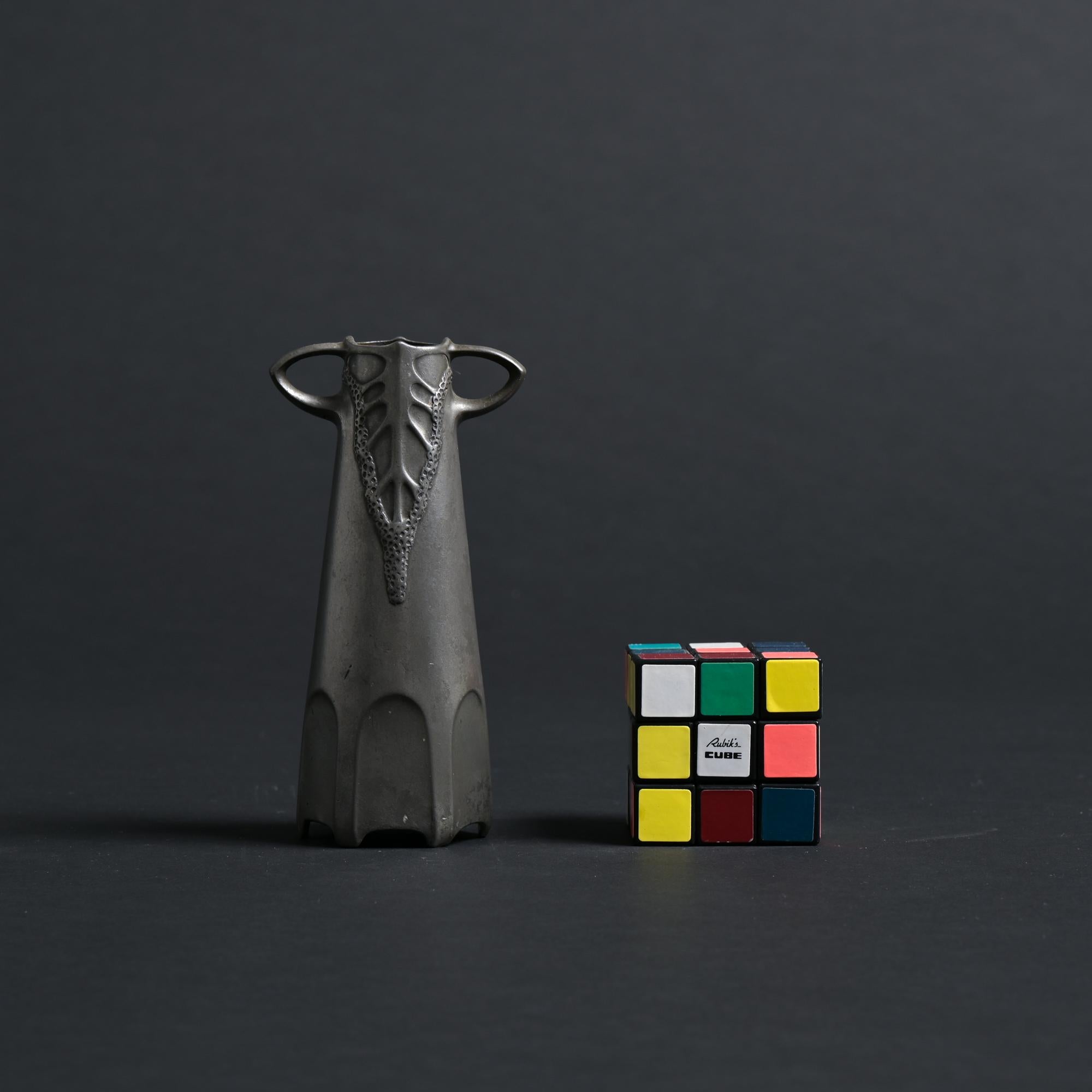 This tin vase was made by the Dutch manufacturer Urania based in Maastricht, Netherlands. The vase is attributed to Friedrich Adler. We date it back to the 1904.

This delicate piece features a floral motive around the neck.

The vase is made out of