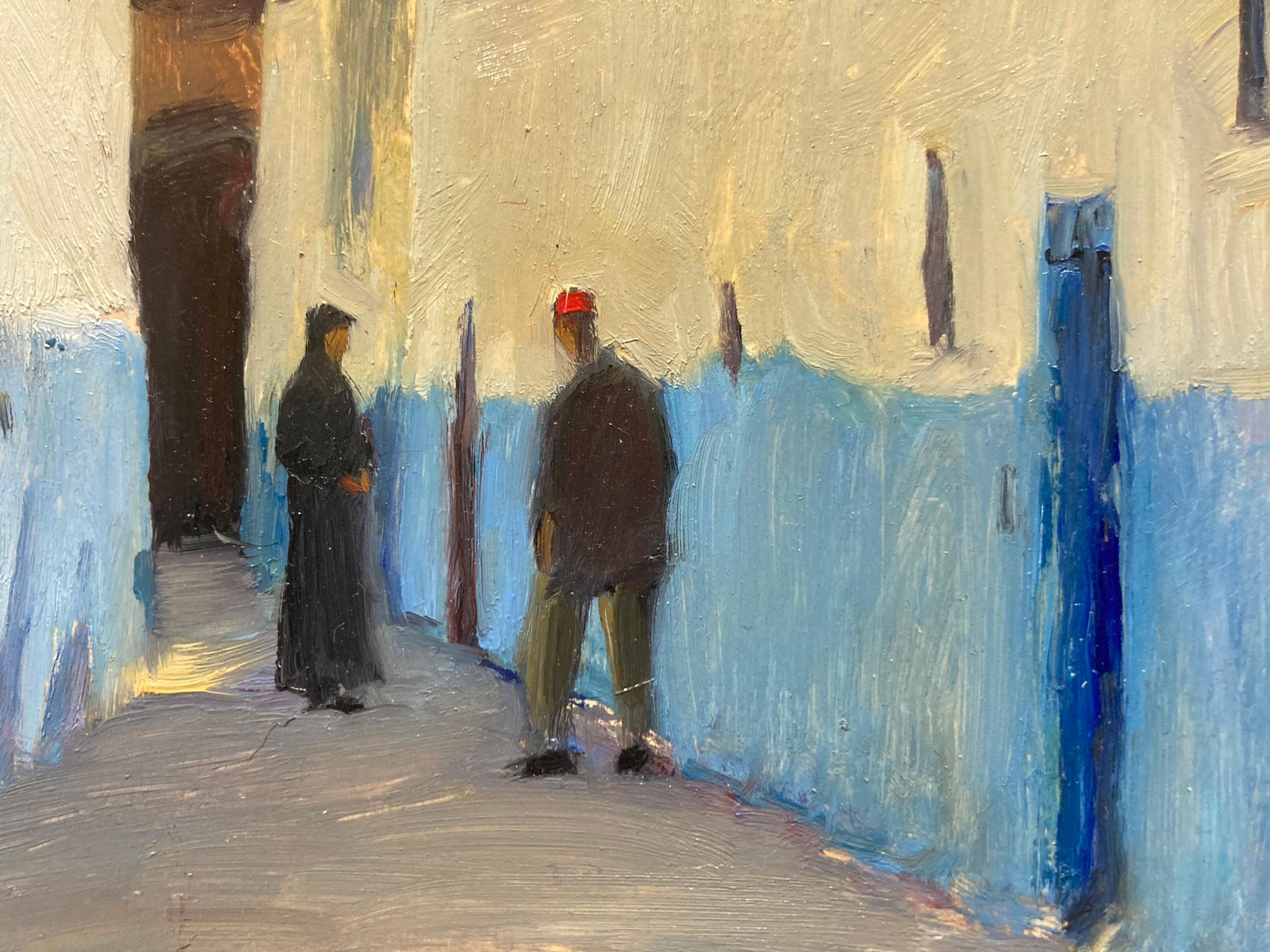 Un colorido cuadro pintado al aire libre de una calle de Marruecos. Dos hombres dan escala a los edificios bellamente decorados. El azul de la base de los edificios inicia un patrón que parece continuarse en el color del cielo, haciéndose más claro