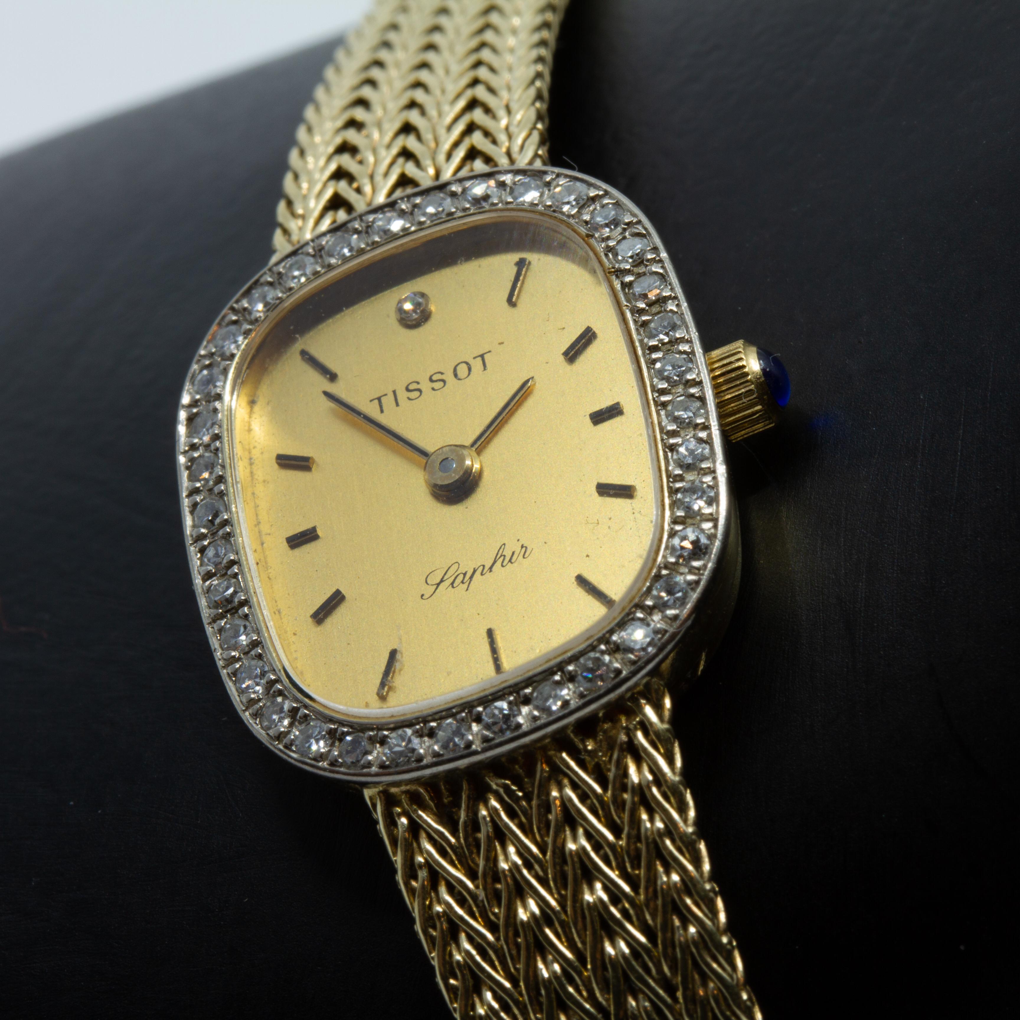 Offeredmis a circa 1980 TISSOT SAPHIR dress-watch, Swiss-made and crafted in subtle 14kt yellow gold. Boasting a sleek cushion-shaped yellow gold dial, with yellow gold and black colored hands, it is attached to a delicate but sturdy 14kt yellow