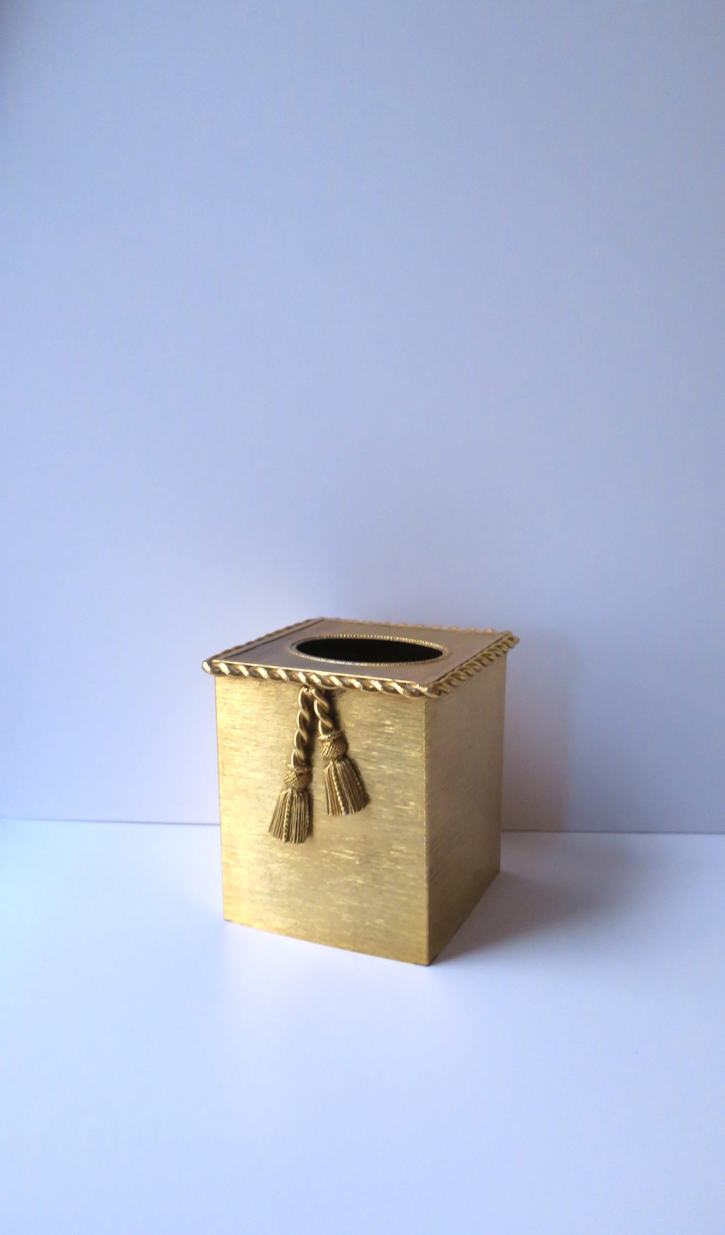A gold metal tissue box cover with twist design around edge and tassel detail, circa mid to late-20th century, USA. Piece is a vibrant gold with a twisted rope detail around exterior top edge and two tassels down front. A great addition to any room,