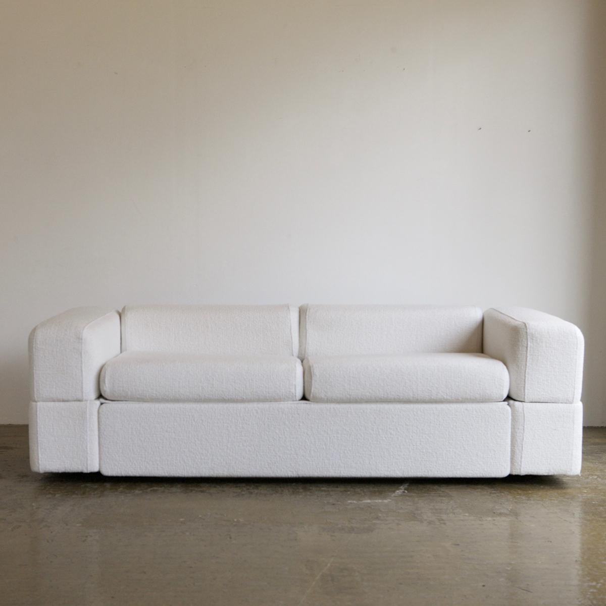 An iconic sofa by Tito Agnoli for Cinova, newly upholstered in a white woven textured wool. A compact and super comfortable piece with a minimalistic design. This version of the Agnoli sofa bed is rare in that a double bed folds out. The arms flip