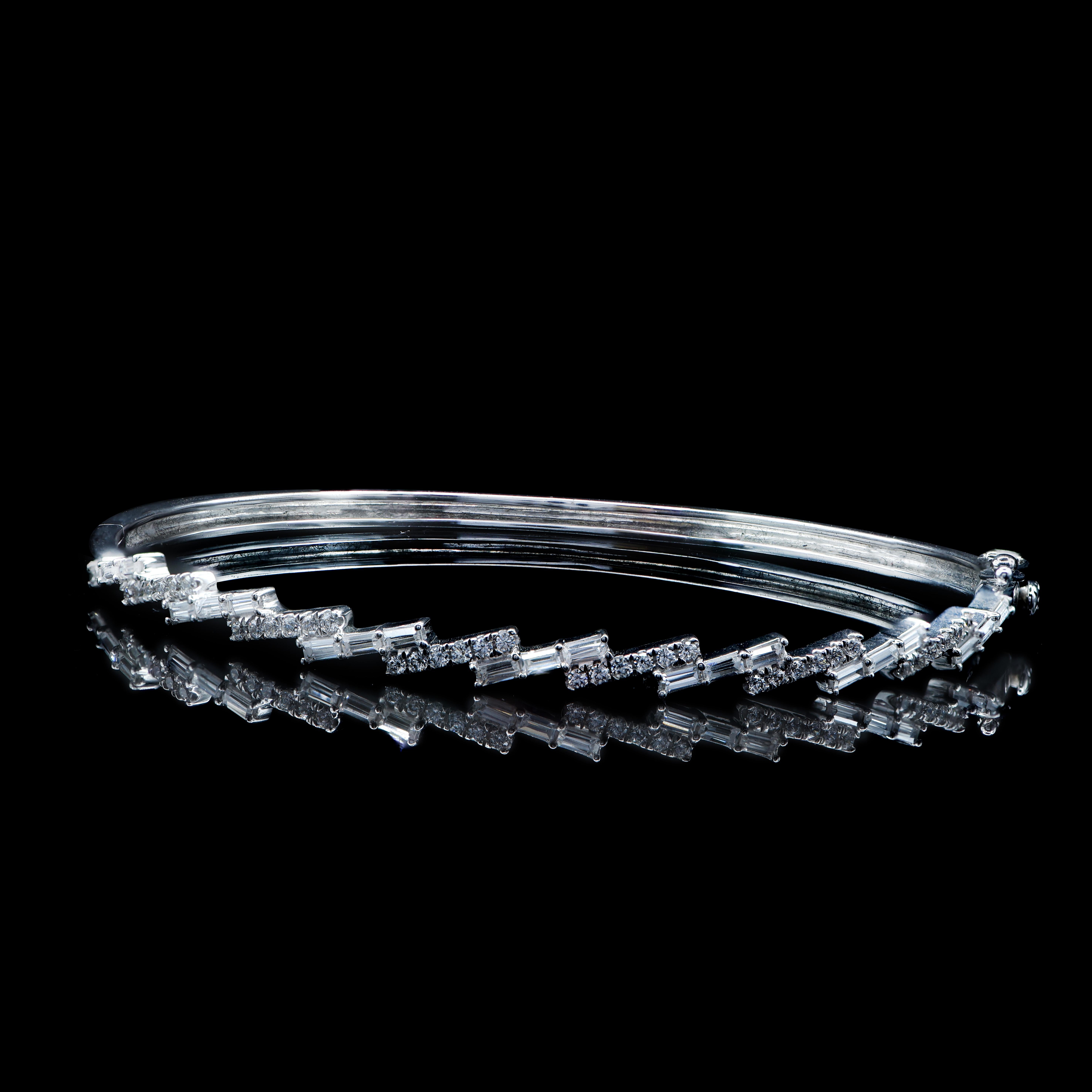 This designer bangle is made by our skillful craftsmen in 18-karat white gold and studded with 36 brilliant cut and 21 baguette-cut diamonds set in micro-prong and prong setting. The diamonds are graded H-I Color, I2 Clarity. 
The diameter of the