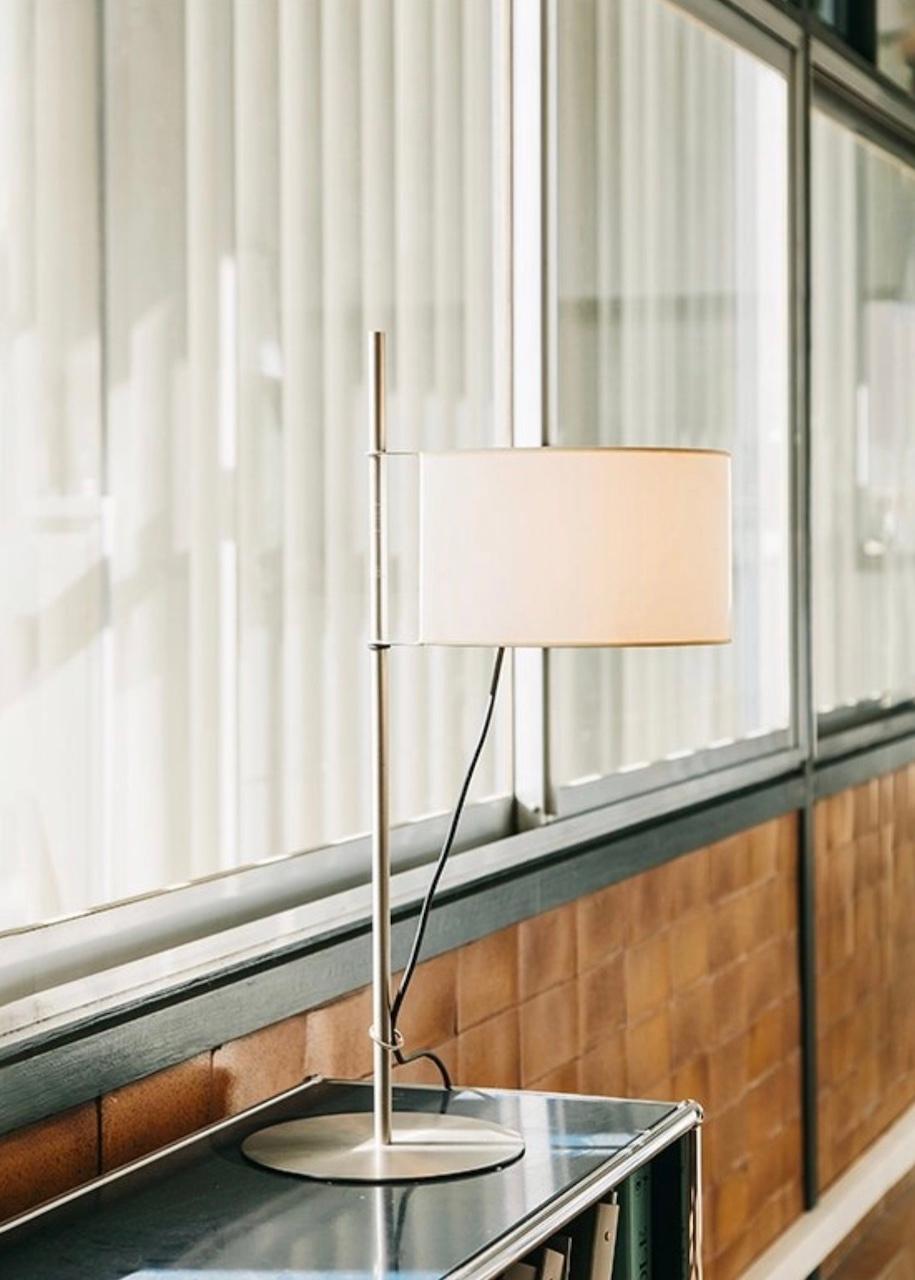 A shade that is hoisted like a sail on a mast. Based on his famous TMM lamp, Miguel Milá was commissioned to design the TMD tabletop version. The designer came up with the idea of a shade that is raised like a flag up a mast. In order to reduce the