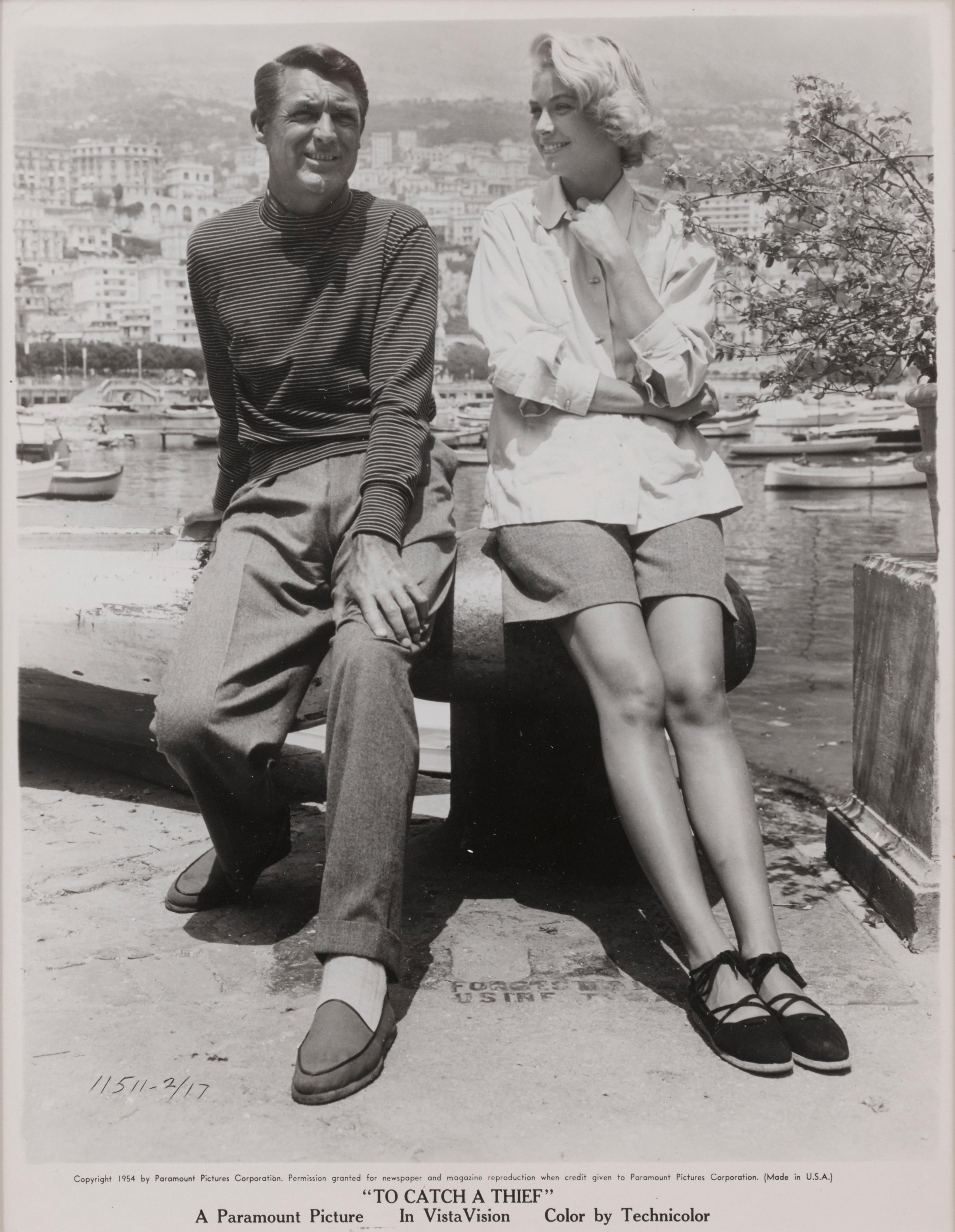 Original candid photographic production still for Alfred Hitchcock's 1955 Thriller To Catch a Thief. This candid photo shows the stars Cary Grant and Grace Kelly relaxing between filming. 
This piece is framed in a Sapele wood frame with acid free