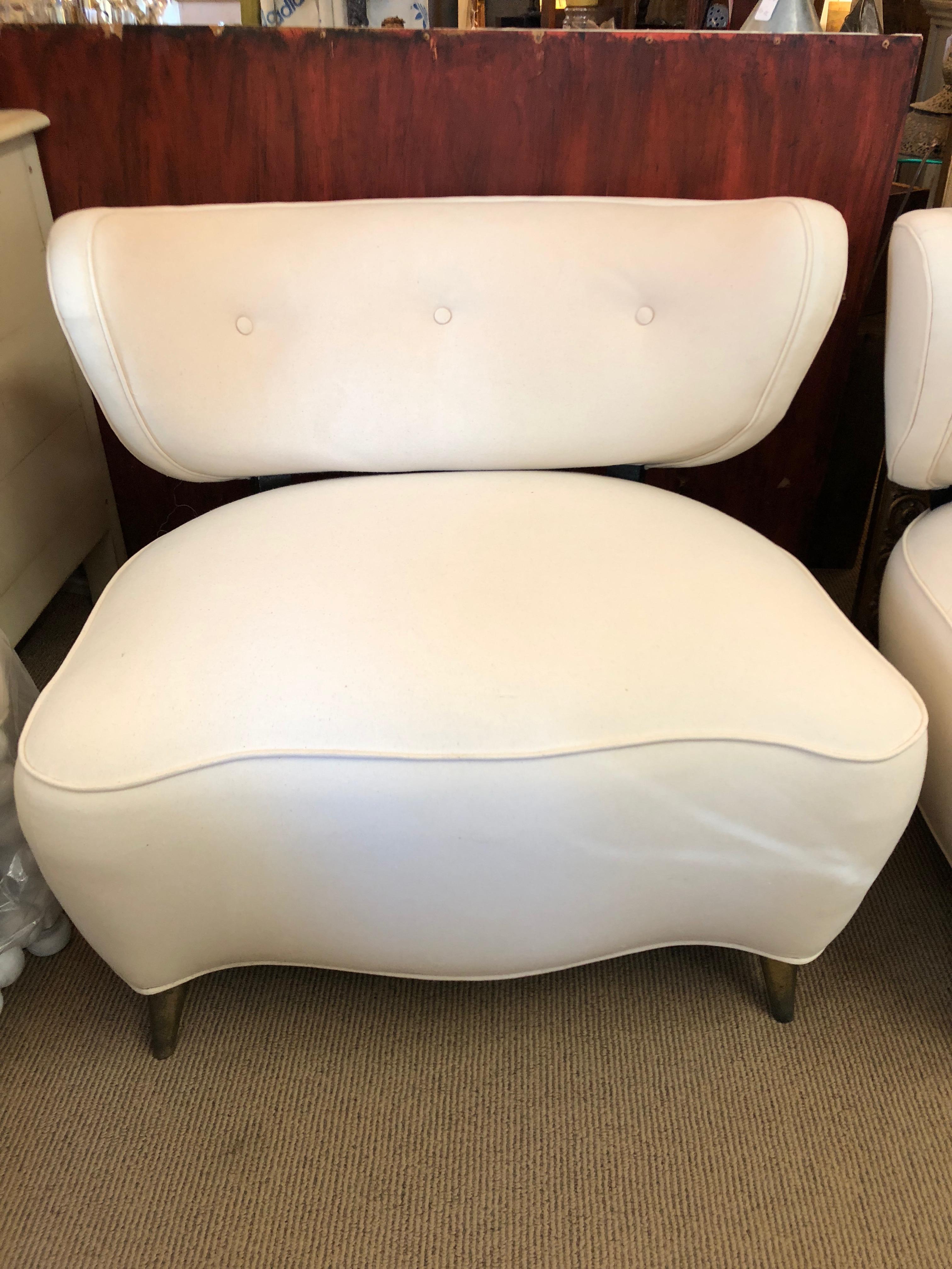 Sexy curvy super stylish pair of French club lounge chairs in the style of Gilbert Rohde having fabulously shaped seats with a scalloped low slung bottom edge and rounded back. Tapered brass feet finish the height of design in these midcentury