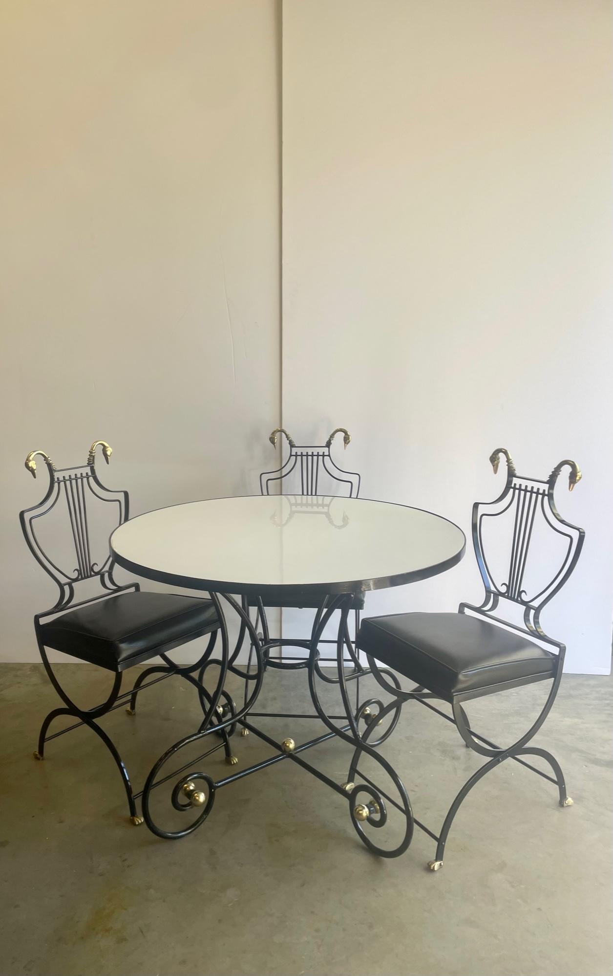 Superbly stylish Maison Jansen round dining table and set of 4 matching chairs having a fabulous black wrought iron decorative curlicue base with brass ball decoration, white milk glass top, and 4 lyre motif iron chairs with swan decoration and