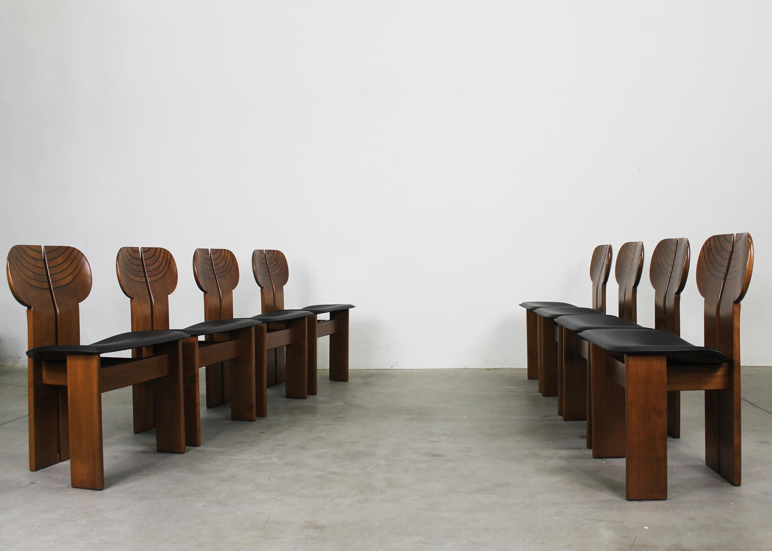 Ensemble de huit chaises africaines avec structure en bois de noyer, assise en cuir noir et détails en laiton. 
Conçu par Tobia et Afra Scarpa et produit par Maxalto dans les années 1970. 

Ces chaises sculpturales uniques ont été conçues par Tobia