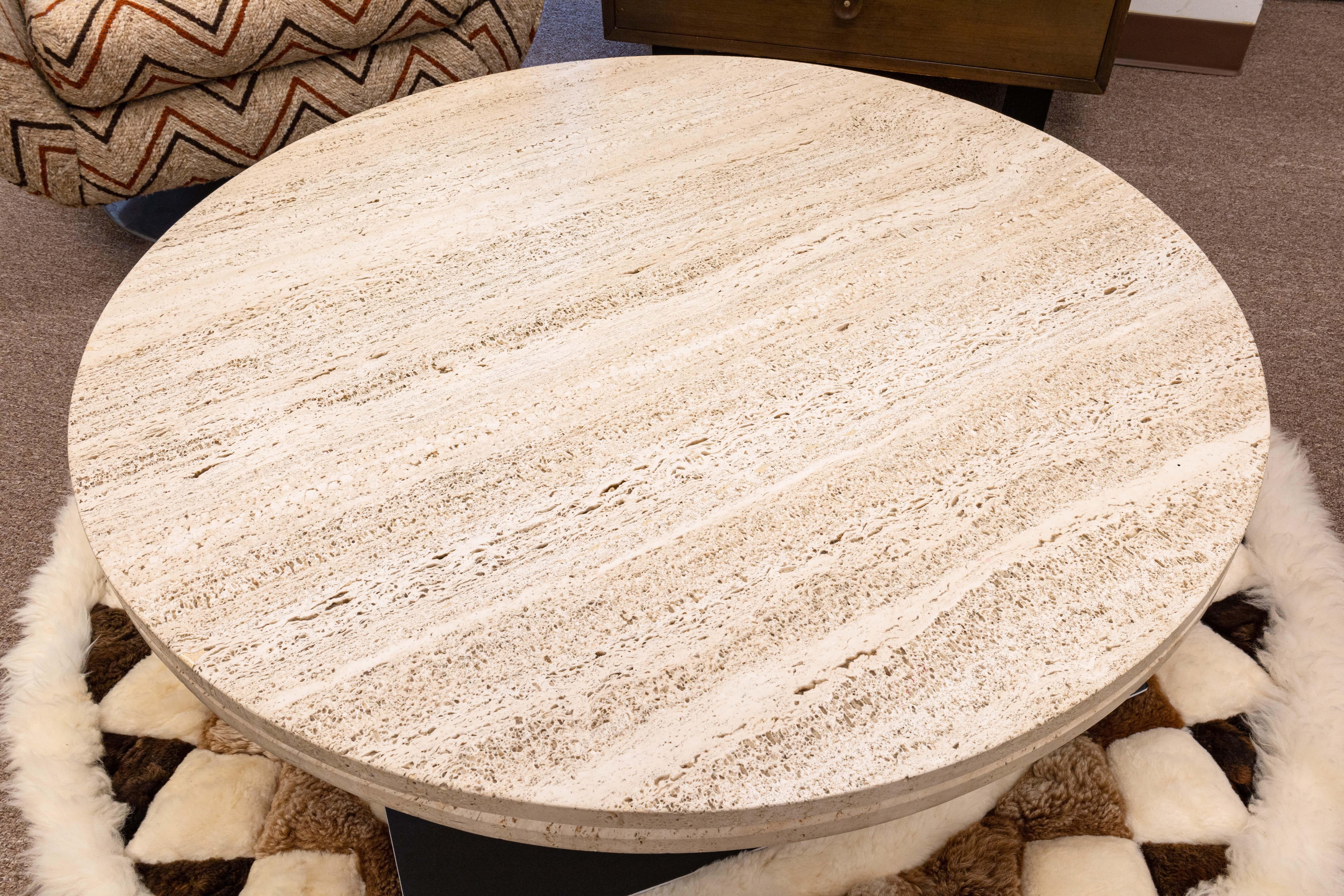 A Tobocman round travertine coffee table. This lovely coffee table features a round travertine table top, and a round wooden base. The travertine has fantastic texture and color variation, and the light wood base compliments the top greatly. This