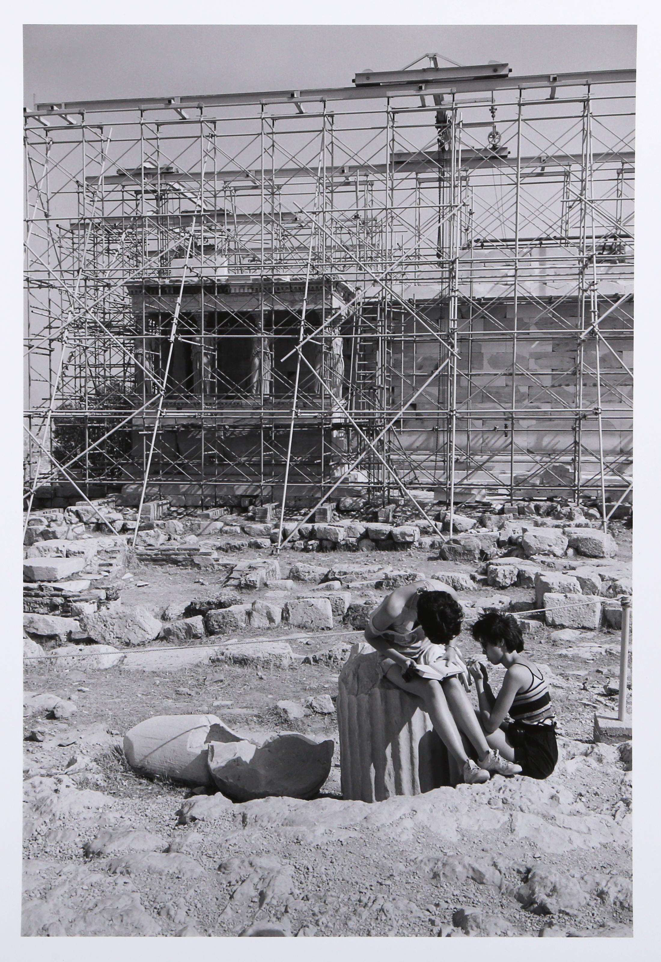 By The Erectheum is a gelatin silver print from On the Acropolis, a portfolio of 25 photographs by Tod Papageorge made on the Athenian Acropolis in the summers of 1983 and 1984. The image depicts two figures sitting huddled at the base of a fallen