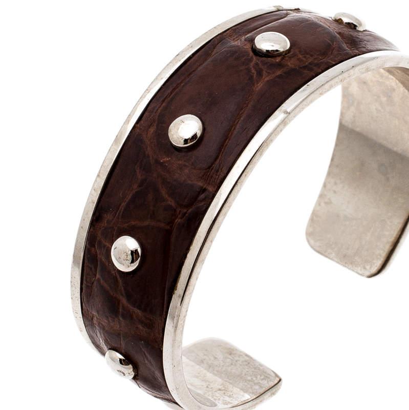 This Tod's bracelet features an open cuff silhouette making it easy to slip in and out. It is fashioned in a wide silver-tone body with brown embossed leather inlay. Completed with stud detailing on the exterior, this simple piece looks best when
