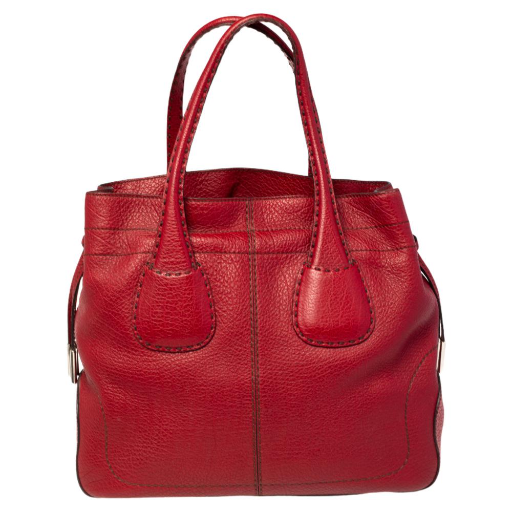 This stylish tote bag comes from the house of Tod's. Crafted in Italy, it is made of quality leather and comes in a lovely shade of red. This bag is held by dual handles and features a drawstring closure. It opens to reveal a spacious nylon interior