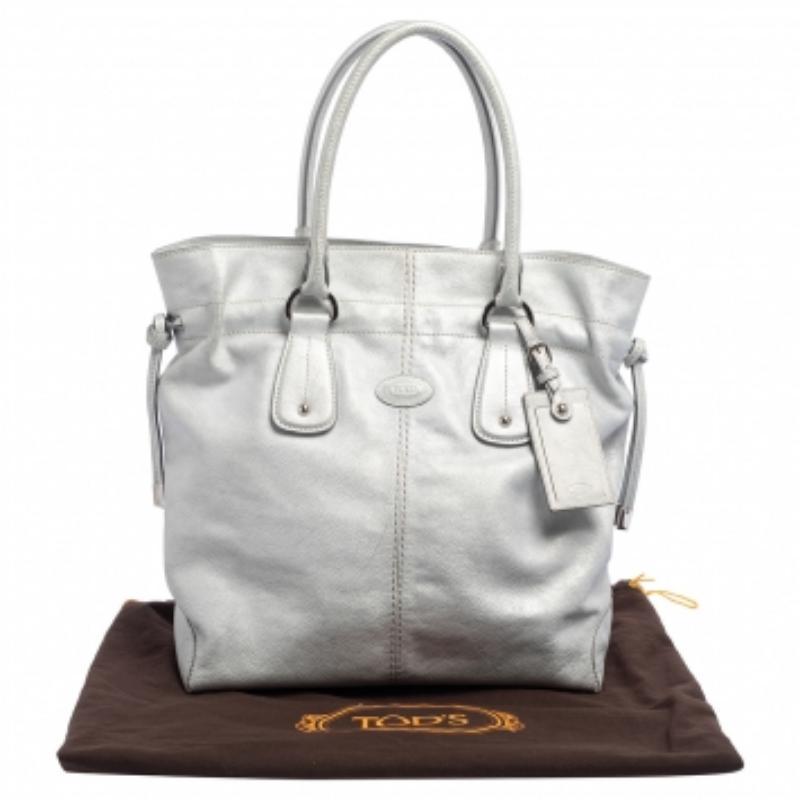 Diese stilvolle Tasche stammt aus dem Hause Tod's. Sie wird in Italien aus hochwertigem Leder gefertigt und ist in einem schönen Silberton gehalten. Die Tasche wird von zwei Griffen gehalten und hat einen Kordelzugverschluss. Das Markenlogo ist auf