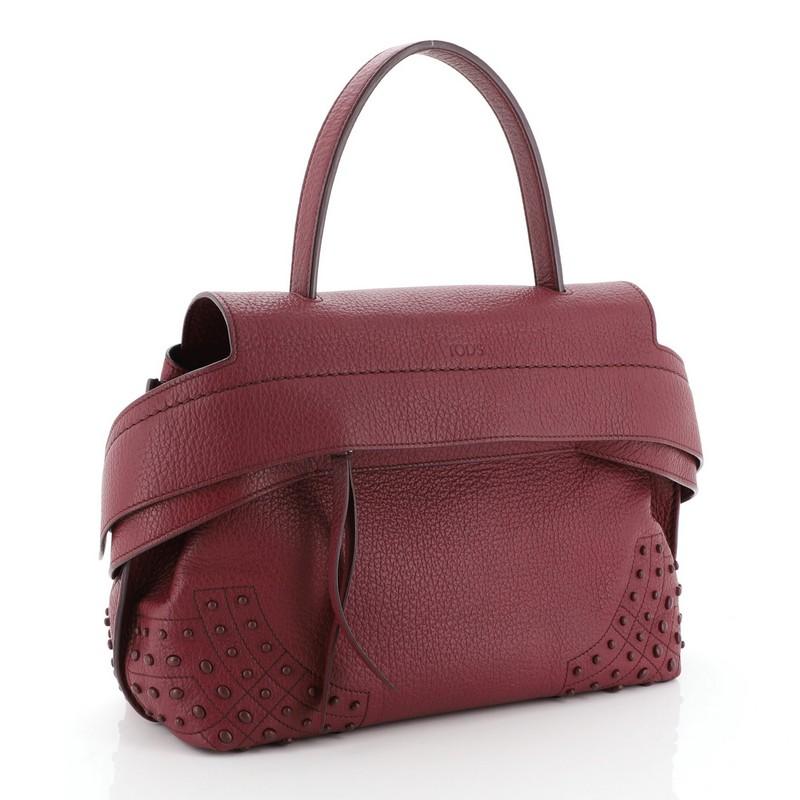 This Tod's Studded Wave Bag Leather Small, crafted from purple leather, features flat leather top handle, wide front leather band with button fastening on the sides, stud detailing on base corners, exterior back pocket with snap closure, and