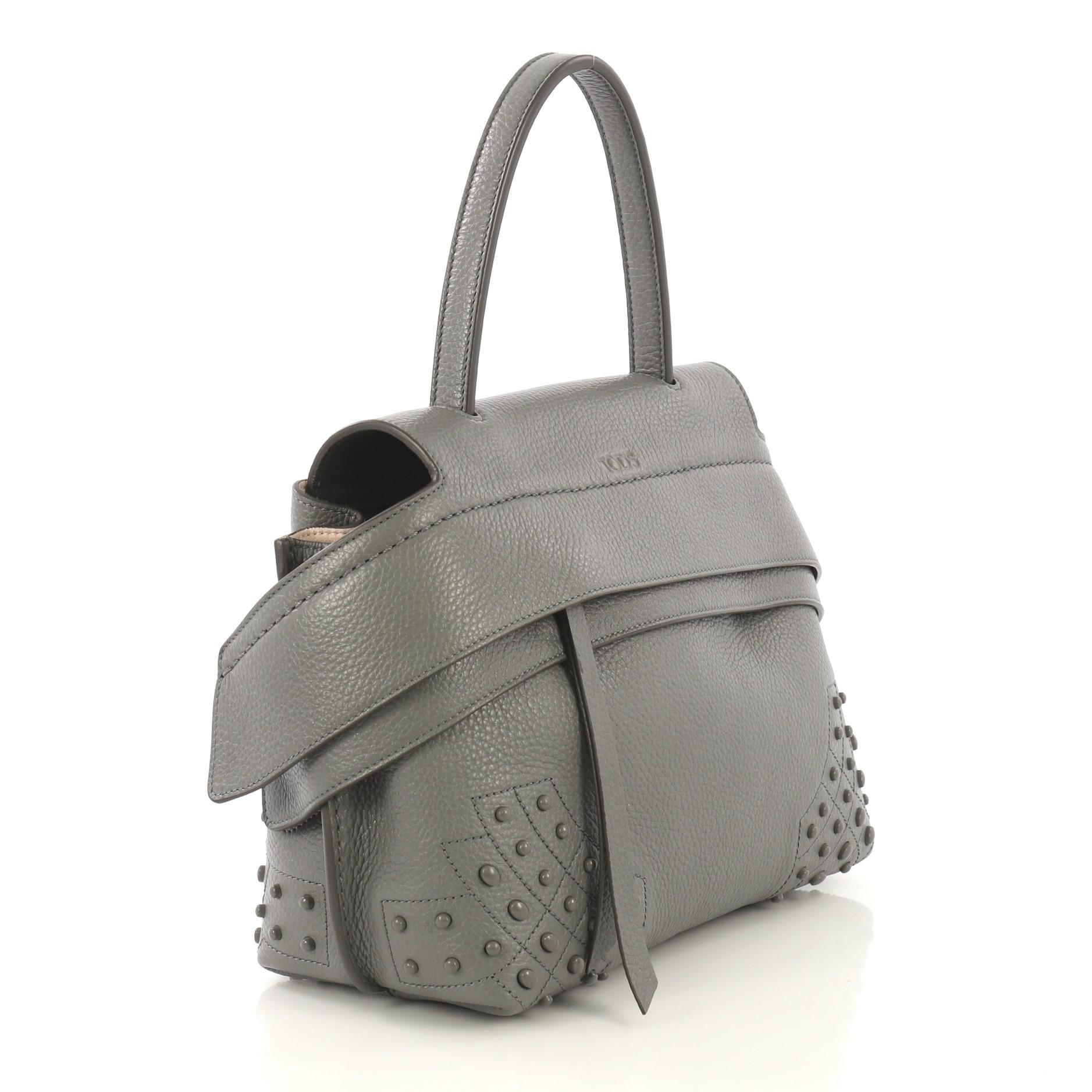 This Tod's Wave Bag Embellished Leather Small, crafted from gray leather, features flat leather top handle, wide front leather band with button fastening on the sides, multiple stud detailing on base corners, exterior back pocket with snap closure,