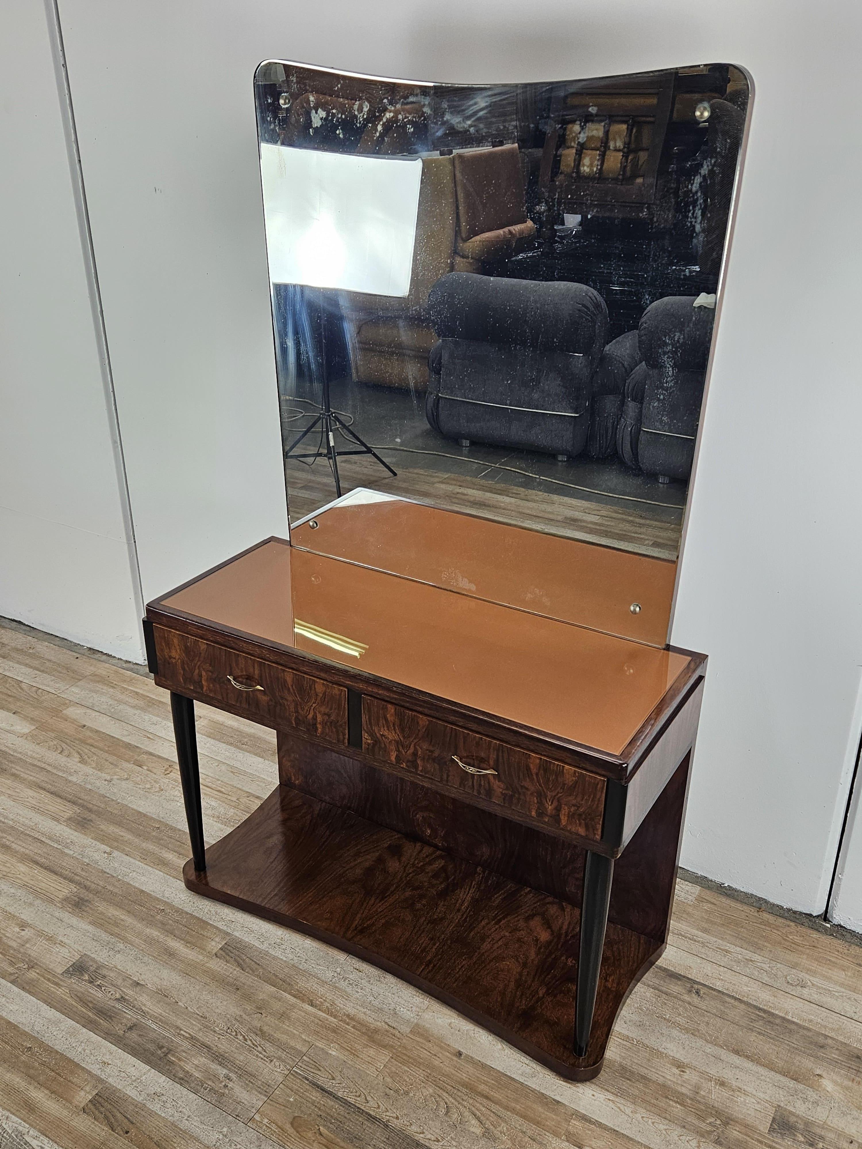 Elégant cabinet de maquillage du début des années 1930 en loupe d'acajou avec détails en ébène et double tiroir.

La coiffeuse est un élément unique avec le grand miroir incurvé qui se trouve derrière elle et son magnifique plateau en verre