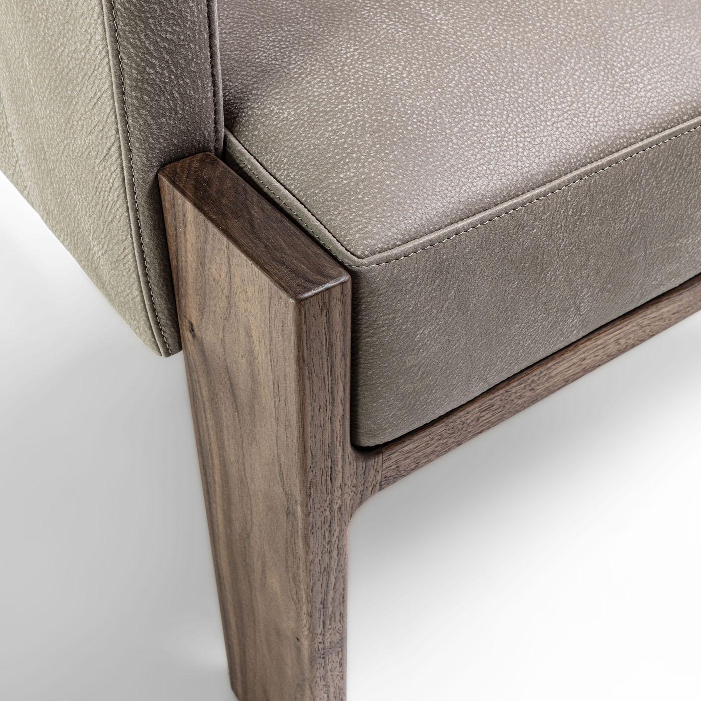 Ein massives Gestell aus Canaletto-Nussbaum mit strengen Profilen verleiht diesem Sessel seine unverwechselbare skulpturale Ausstrahlung. Für höchsten Komfort sorgt die gepolsterte Schale, die von edlem, taupefarbenem Leder umhüllt wird, das an den