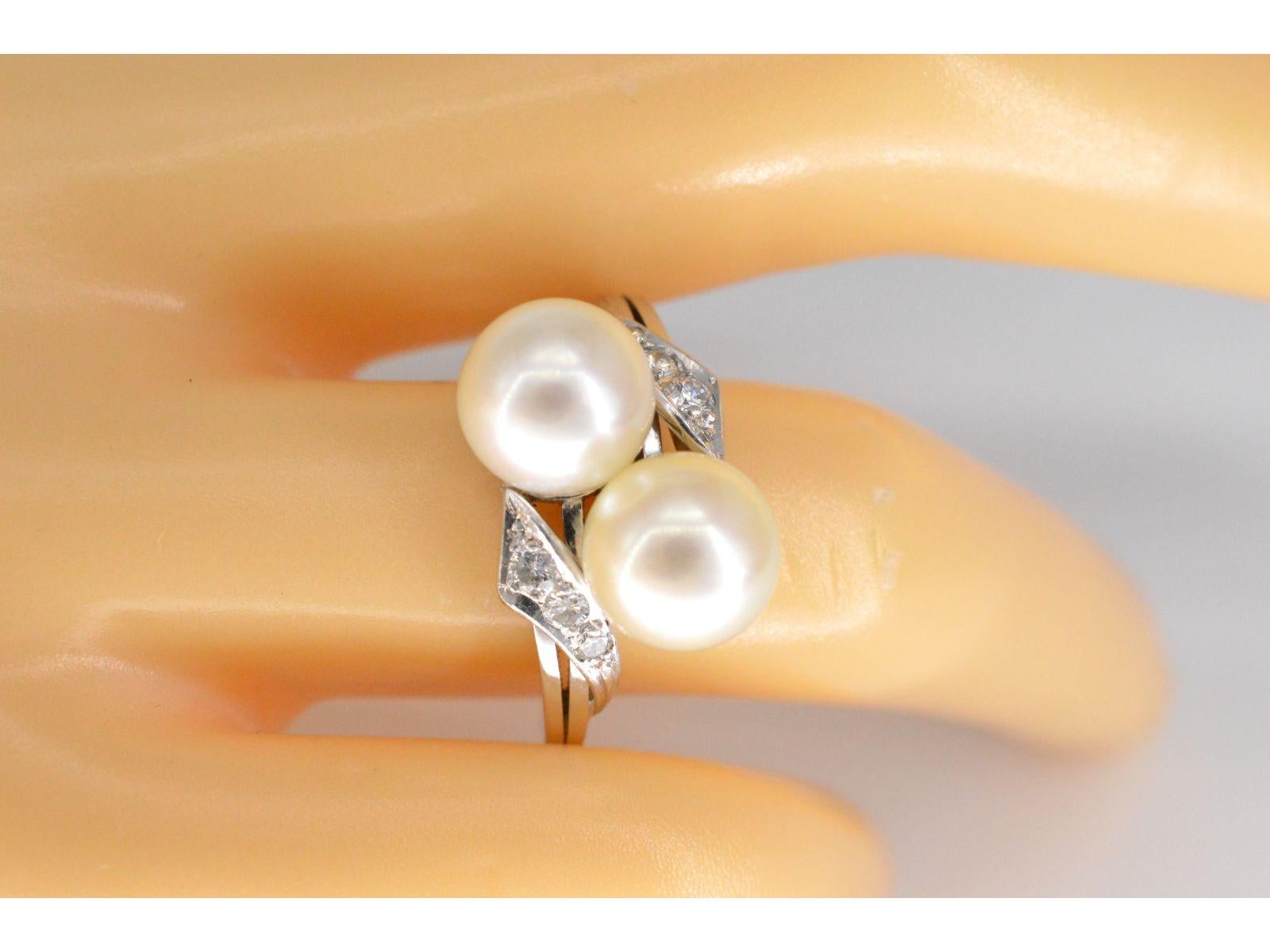 This vintage ring features two stunning pearls with a white-pink-cream color, each measuring 8 mm. The brilliance is enhanced by six brilliant-cut diamonds, totaling 0.18 carats, showcasing F-G color and VS clarity. Weighing 5.5 grams, the ring is