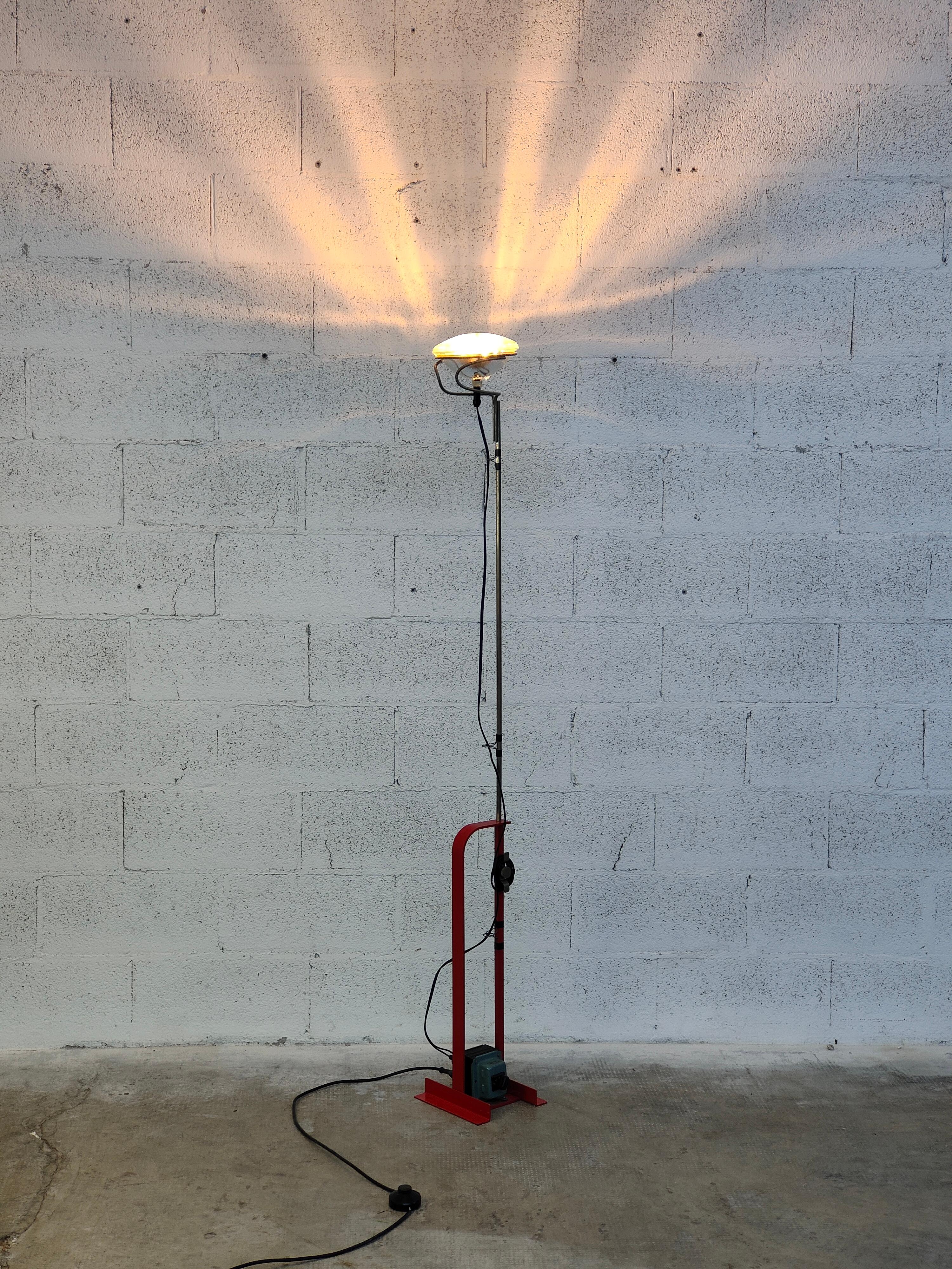 Indirect light floor luminaire. Base in sheared and folded steel and structure in steel sections, both liquid painted. Stem with hexagonal section in nickel-plated brass. The telescopic movement of the rod allows the height of the device to be