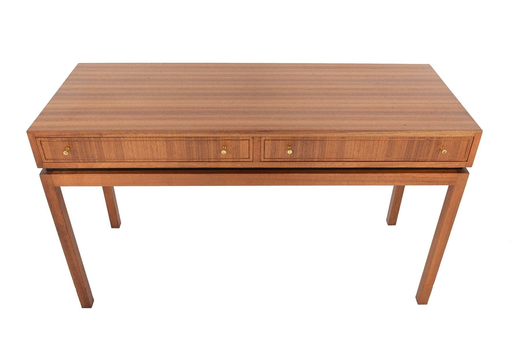 This English modern midcentury console table was designed by Greaves + Thomas in the late 1960s. The beautiful tola case houses two drawers with brass pulls. Stands on tall, mahogany tapered legs. In excellent original condition with typical wear