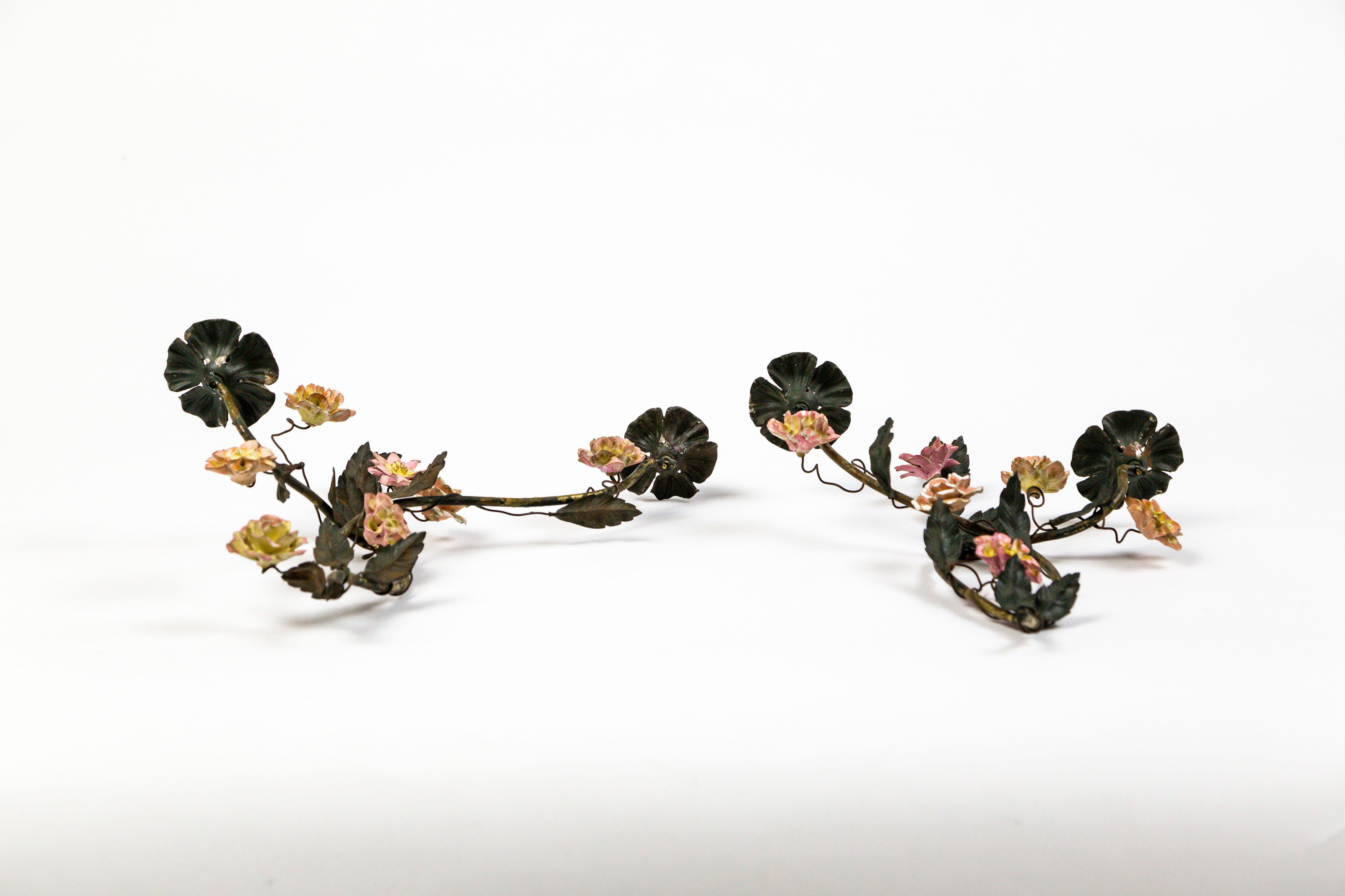 A pair of antique, French tole candle holders of intertwining vines; with dusty pink, yellow, and white porcelain roses, dahlias, and carnations.  Brass structure and mixed metal ornaments with deep green, chipped paint, and aged patina.  Circa
