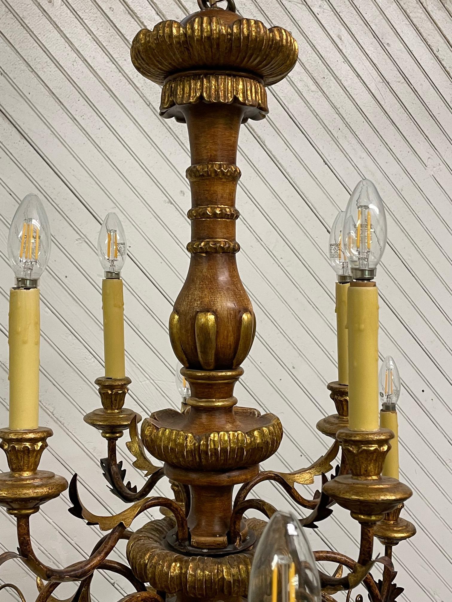 Large 12-arm chandelier features two levels, gold leaf detailing, and tole metal acanthus leaf accents. Good condition with imperfections consistent with age. Some candle sleeves show cracks along top edge. May exhibit scuffs, marks, or wear, see