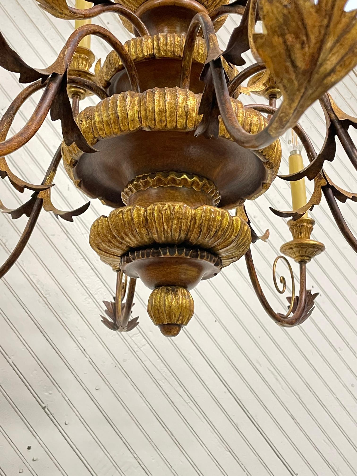 Large 12-arm chandelier features two levels, gold leaf detailing, and tole metal acanthus leaf accents. Good condition with imperfections consistent with age. Some candle sleeves show cracks along top edge. May exhibit scuffs, marks, or wear, see