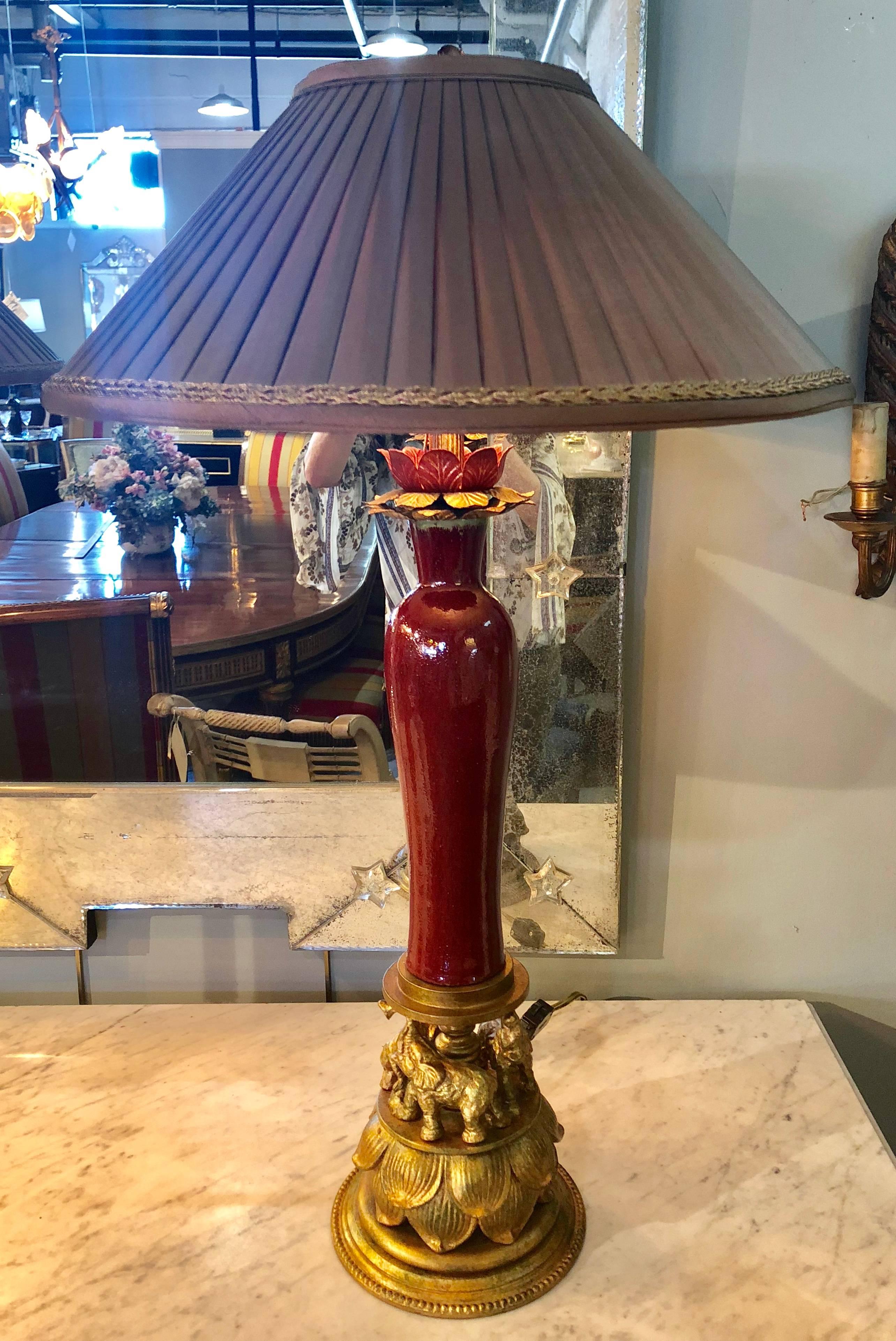 Pair of tole metal red glaze table lamps on gilt elephant bases Signed F. Cooper. This Hollywood Regency style pair of table lamps are certain to add discussion when viewed. The gilt wooded circus elephants pulling the large tent column formed vase
