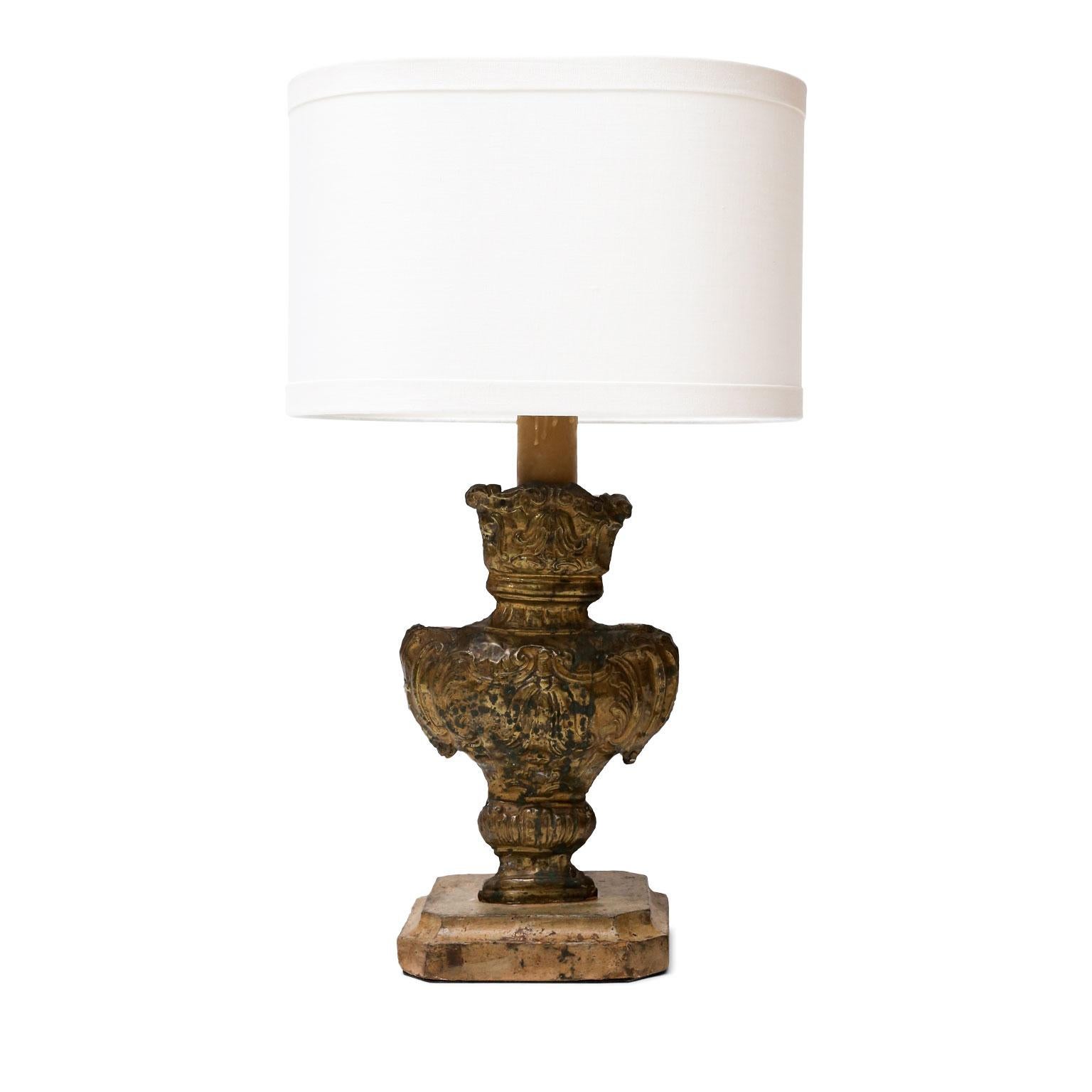 Tole repousse table lamp, newly-wired for use within the USA. 18th century tole repousse decoration applied to an early hand carved urn-shape fragment. Sold with a complementary oval linen shade (measurements in shade).