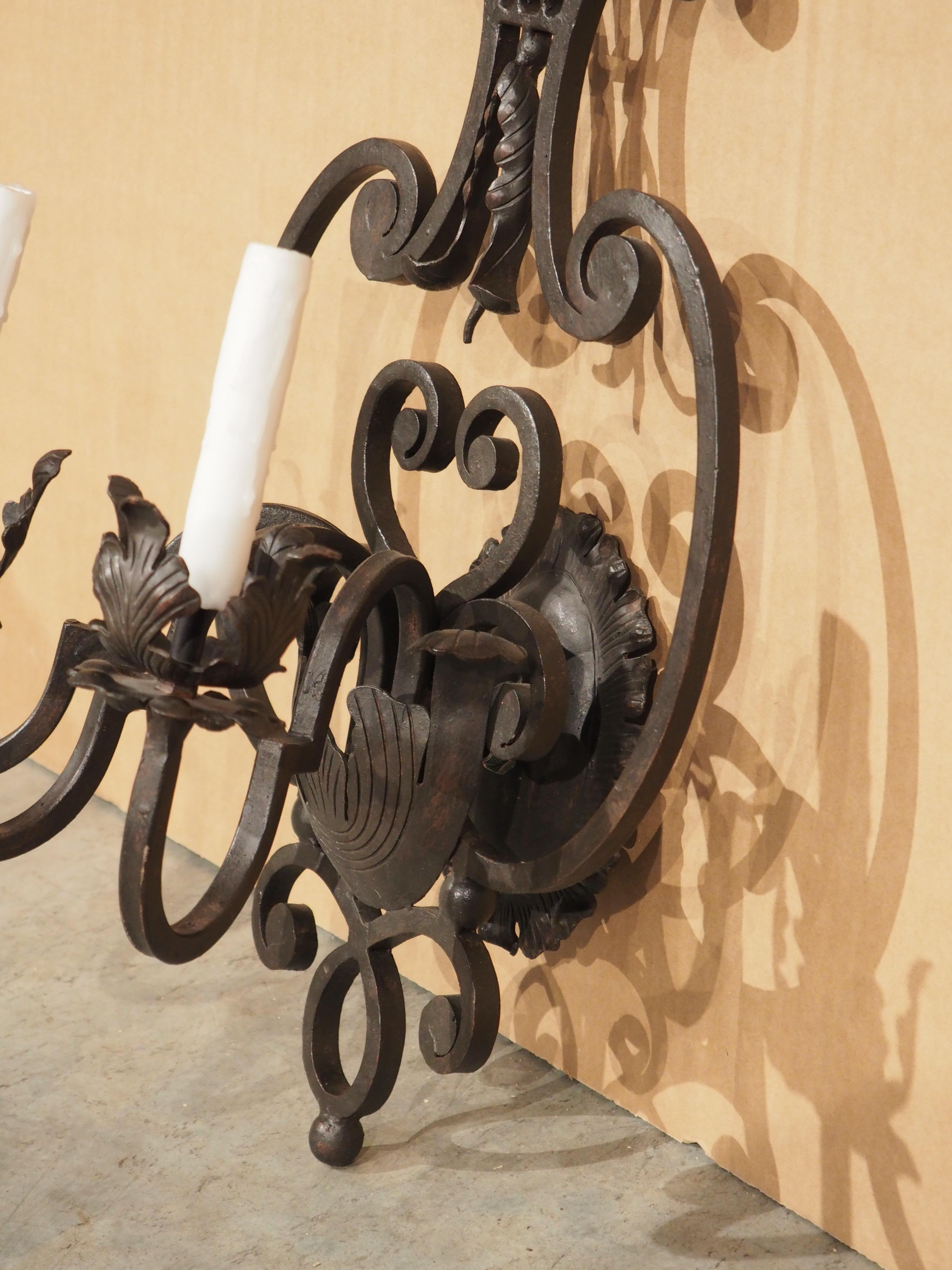 A functional and beautiful three-light wall sconce, wrought by hand to resemble antique Spanish lighting. The three sinuous arms with angular transitions emerge from a leaf cup above a parted backplate. A series of scrolls and a nyctinastic leaf
