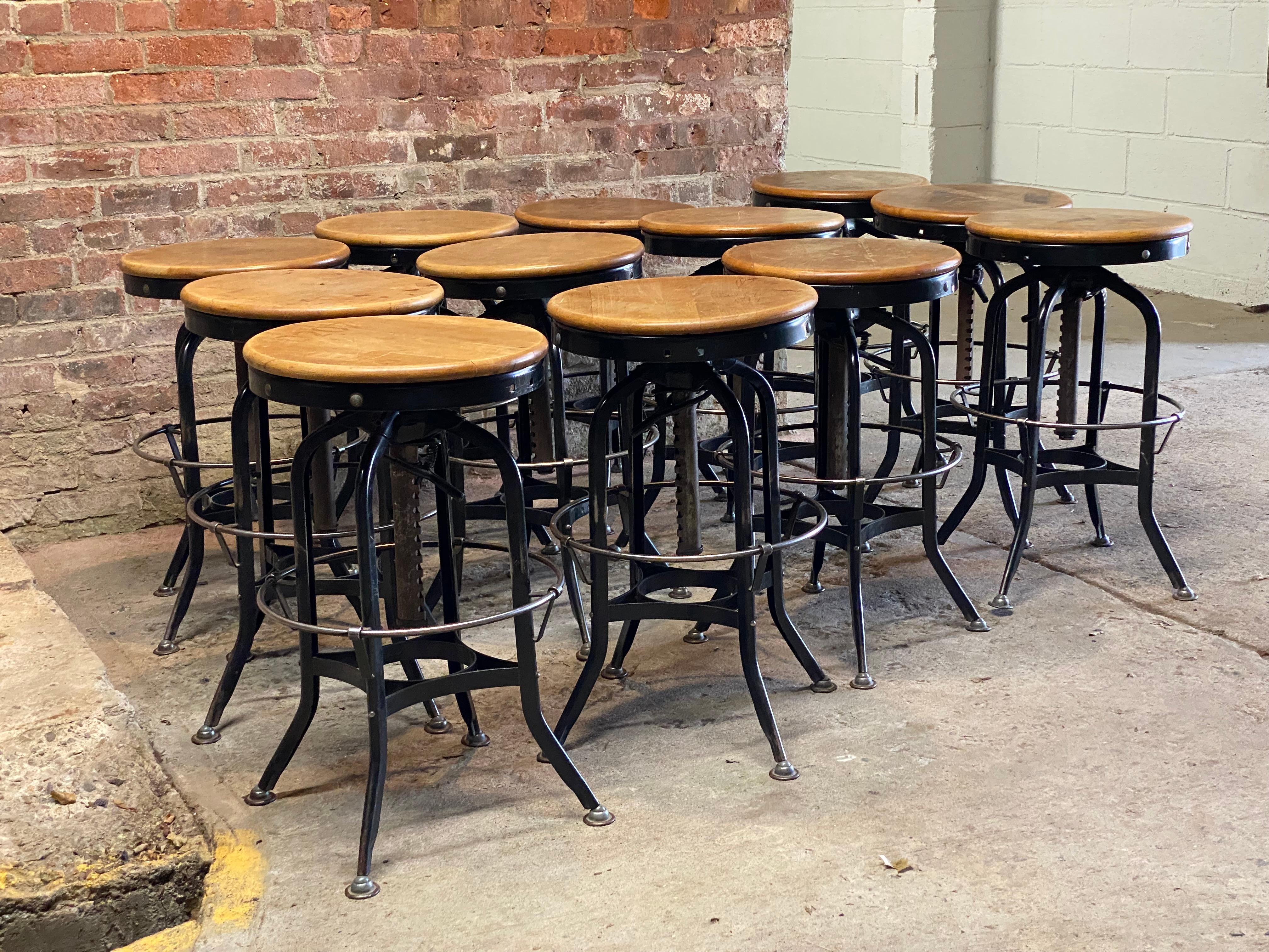 A large set of twelve Toledo industrial adjustable height drafting stools. Steel construction with maple swivel seats. The height is adjustable from approximately 25.5