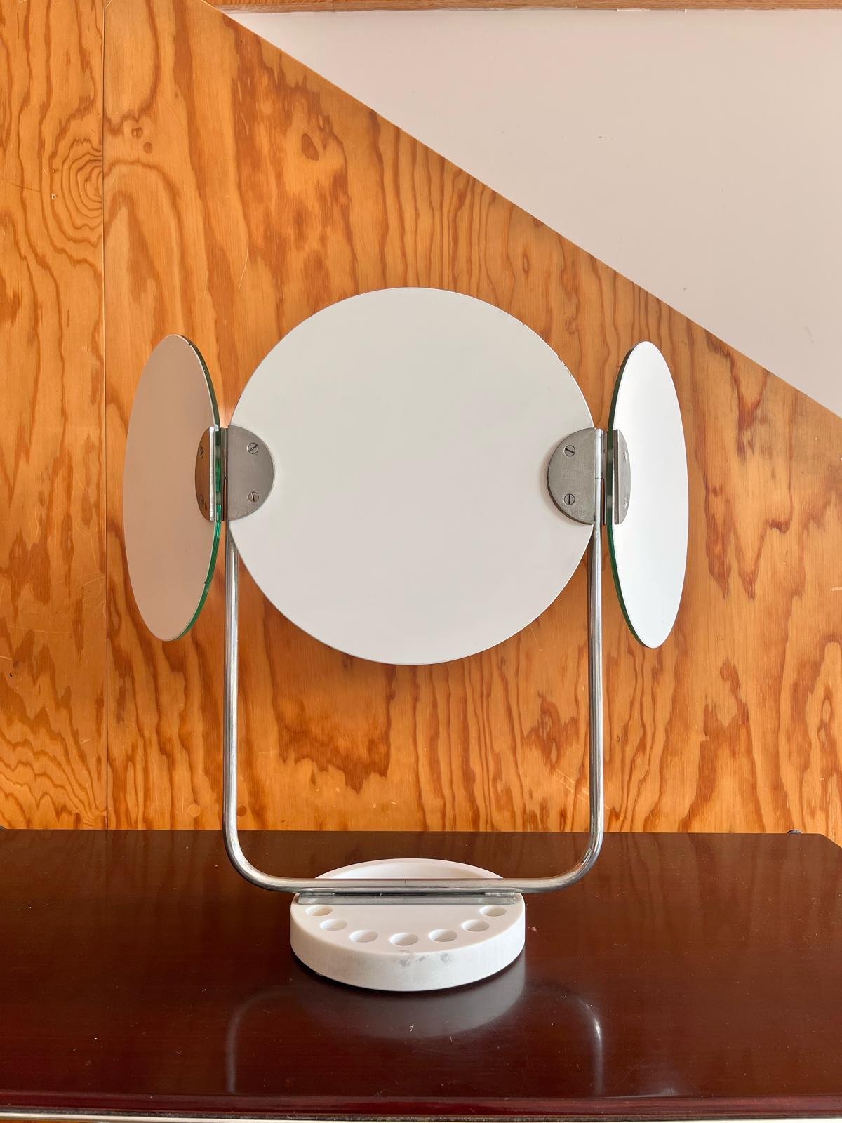 Toletta da tavolo con base in marmo di Carrara, anni '60
Elegante toletta da tavolo realizzata negli anni '60, con base in marmo bianco di Carrara e struttura in acciaio cromato. La toletta è composto da tre specchi tondi richiudibili, di cui uno