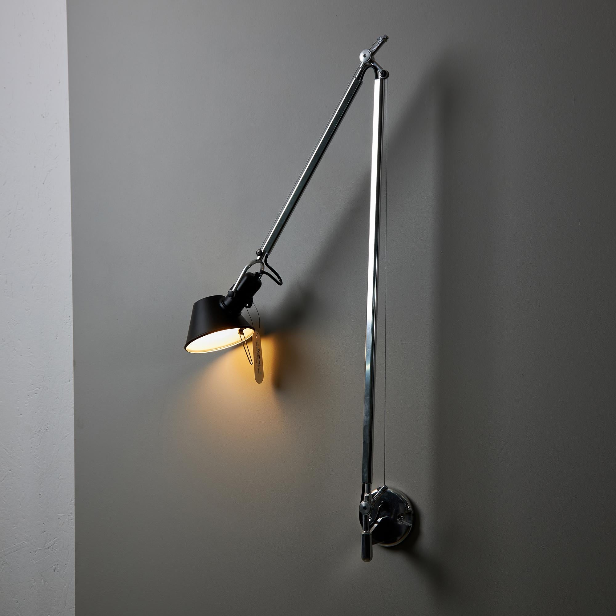 Die Tolomeo Braccio, entworfen von Giancarlo Fassina und Michele de Lucchi, ist eine zeitlose Wandleuchte des italienischen Herstellers Artemide. Sie hat verstellbare Arme aus glänzendem Aluminium, einen schwarzen Polycarbonatdiffusor, der in