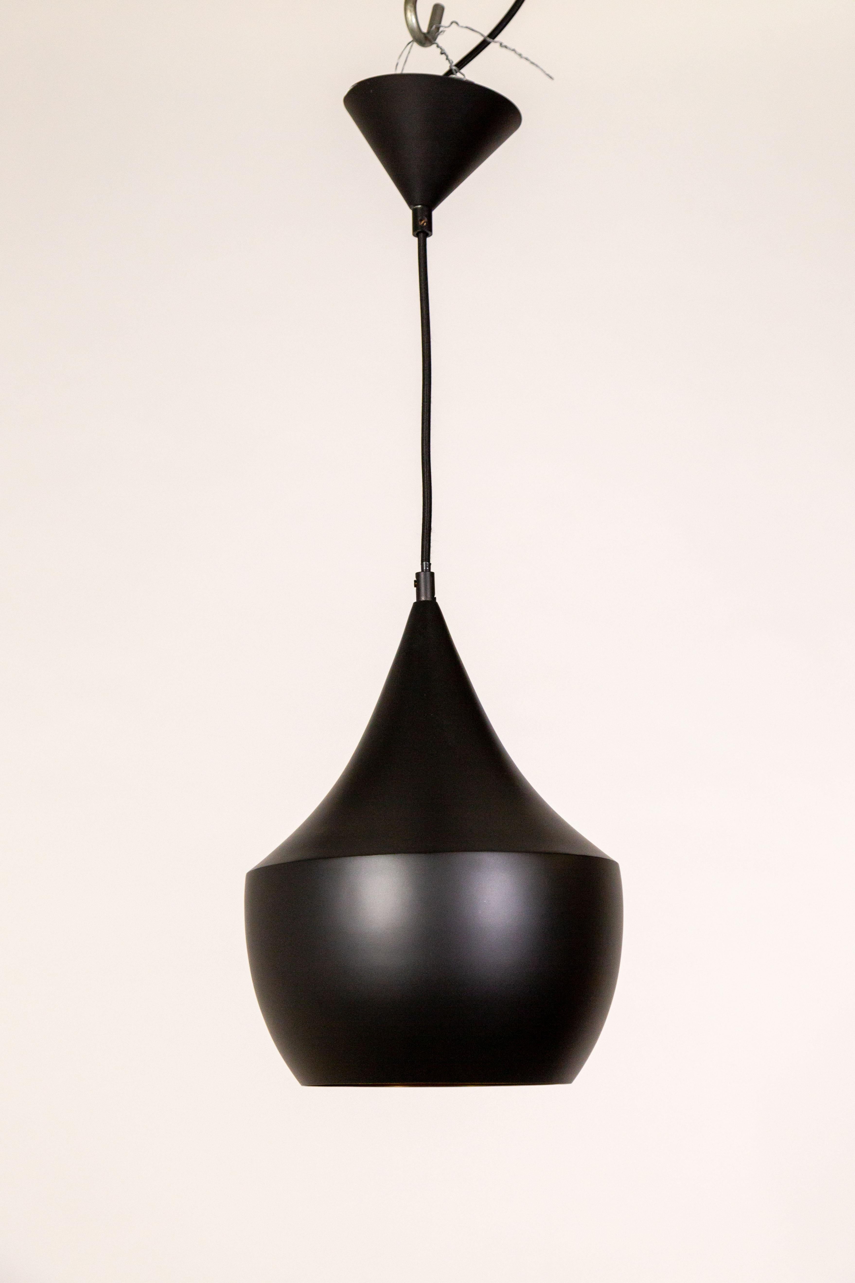 The contemporary Beat Fat pendant light, designed by Tom Dixon, is made of hand spun brass in India. It is satin matte black with a shiny, gold textured interior which refracts and reflects light. With an integrated LED module and black fabric
