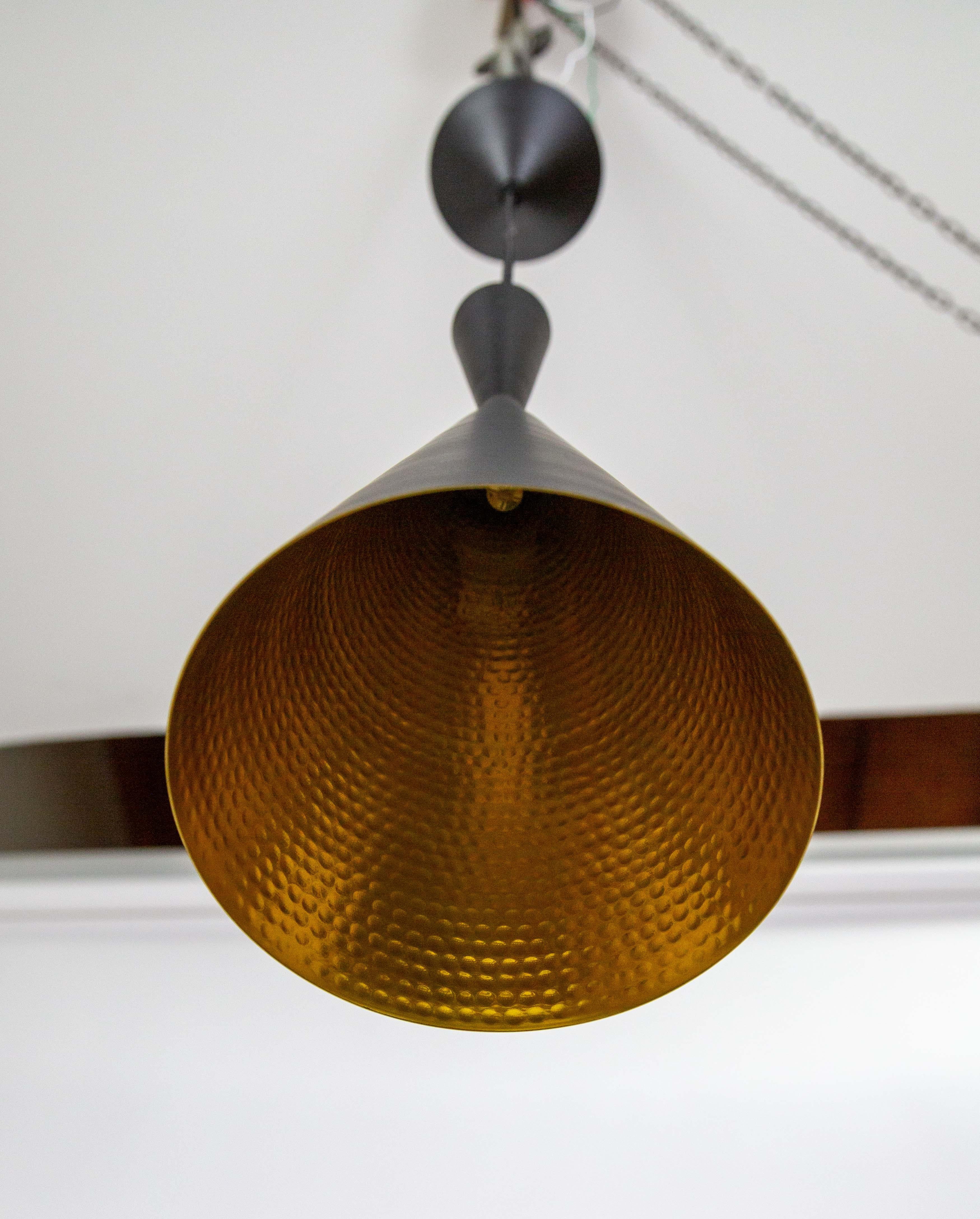 The contemporary Beat Tall pendant light, designed by Tom Dixon, is made of hand spun brass in India. It is satin matte black with a shiny, gold textured interior which refracts and reflects light. With an integrated LED module and black fabric