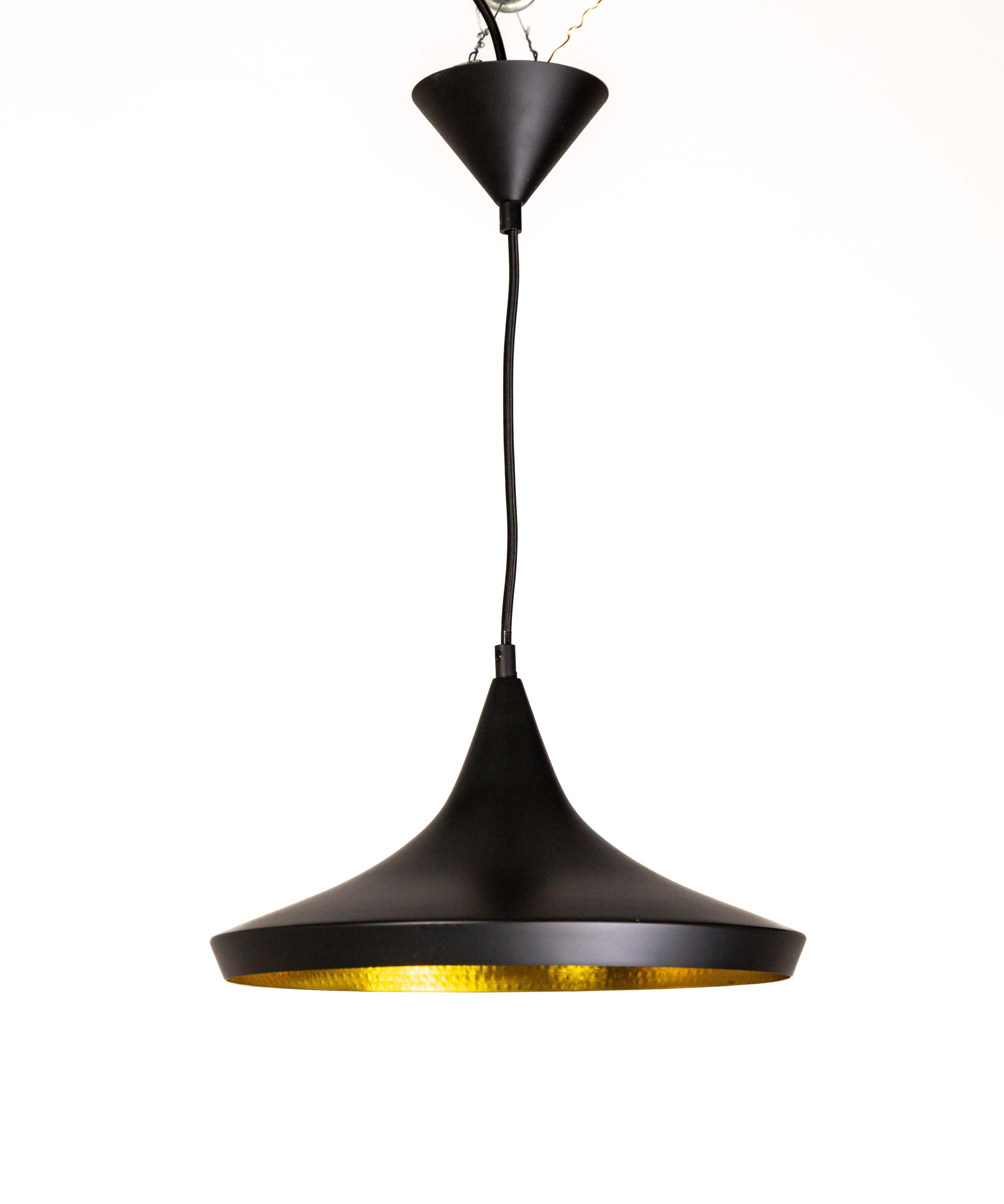 The contemporary Beat Fat pendant light, designed by Tom Dixon, is made of hand-spun brass in India. It is satin matte black with a shiny, gold textured interior that refracts and reflects light. With an integrated LED module and black fabric