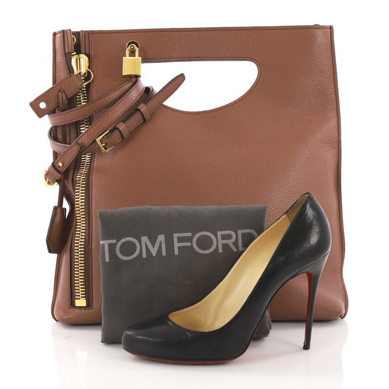 This Tom Ford Alix Fold Over Crossbody Bag Leather, crafted from brown leather, features a cutout top handle, exterior back zip pocket, vertical front zip, and gold-tone hardware. Its fold-over top opens to a brown microfiber interior with a side