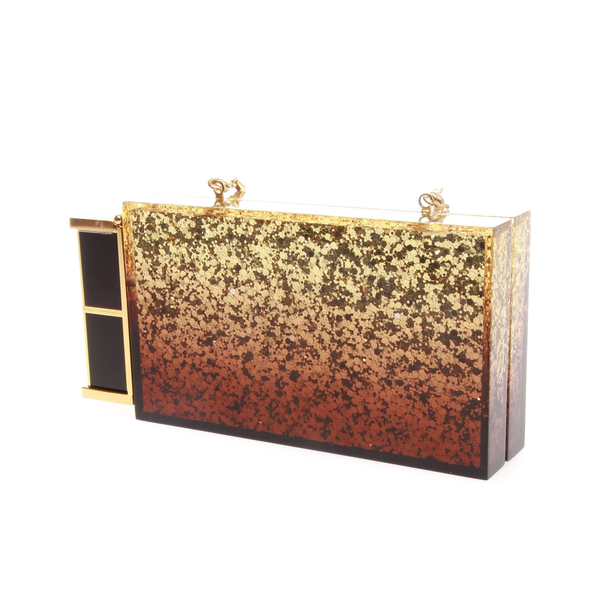 Tom Ford Gold Glittered Plexi-glass Clutch
A Glamorous clutch with a twist, the 'Lipstick' from Tom Ford is a clever piece that you will fall in love with.
Crafted from glittered smoke plexiglass and attached with Tom Ford's lipstick (shade Vanilla