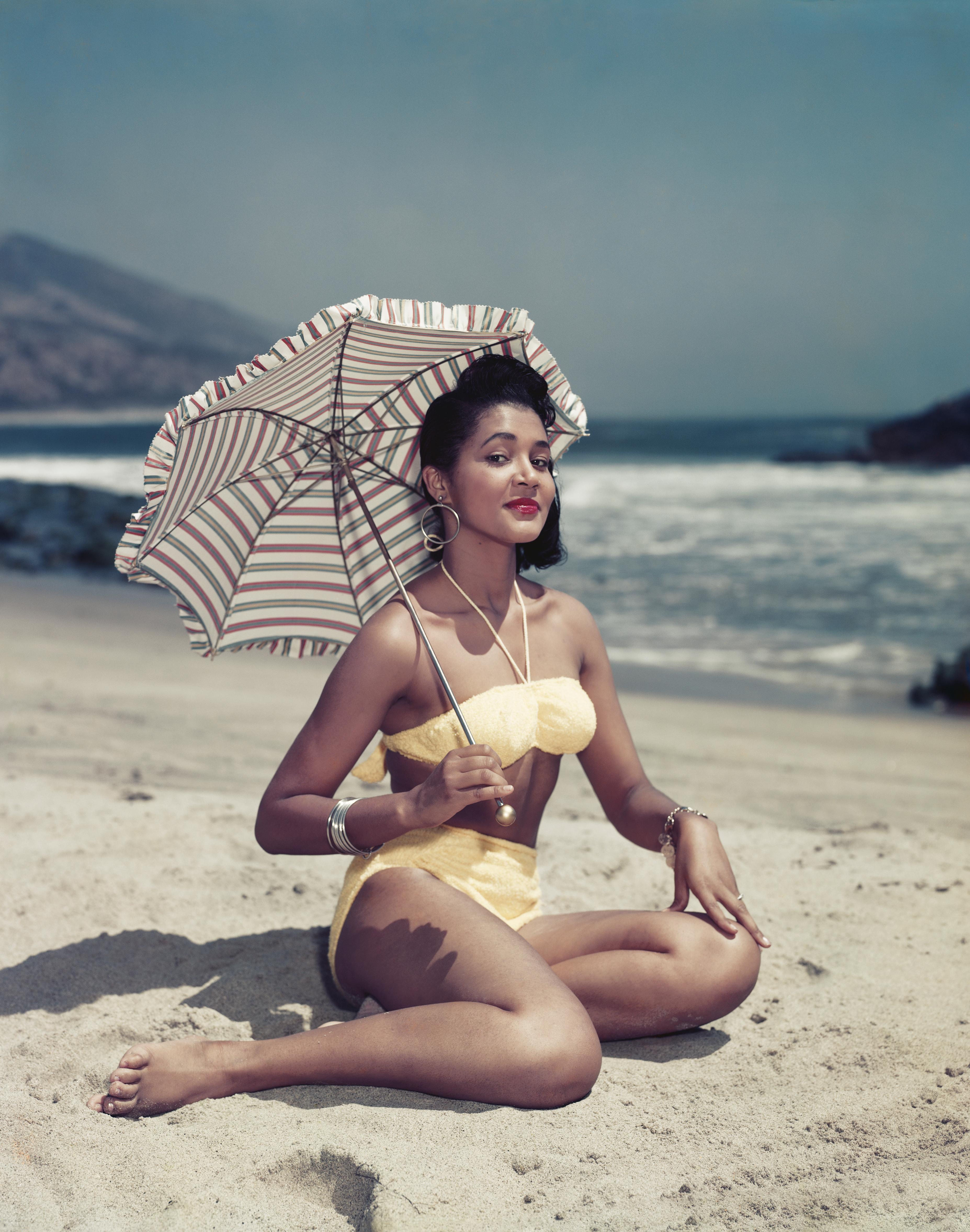 Tom Kelley
Woman With Umbrella
c. 1950's
C print
38 x 32 inches 

Caption: Woman in bikini sitting on beach holding umbrella, smiling, portrait. 

Tom Kelley’s interesting career spans more than four decades: first started as an apprentice in a New
