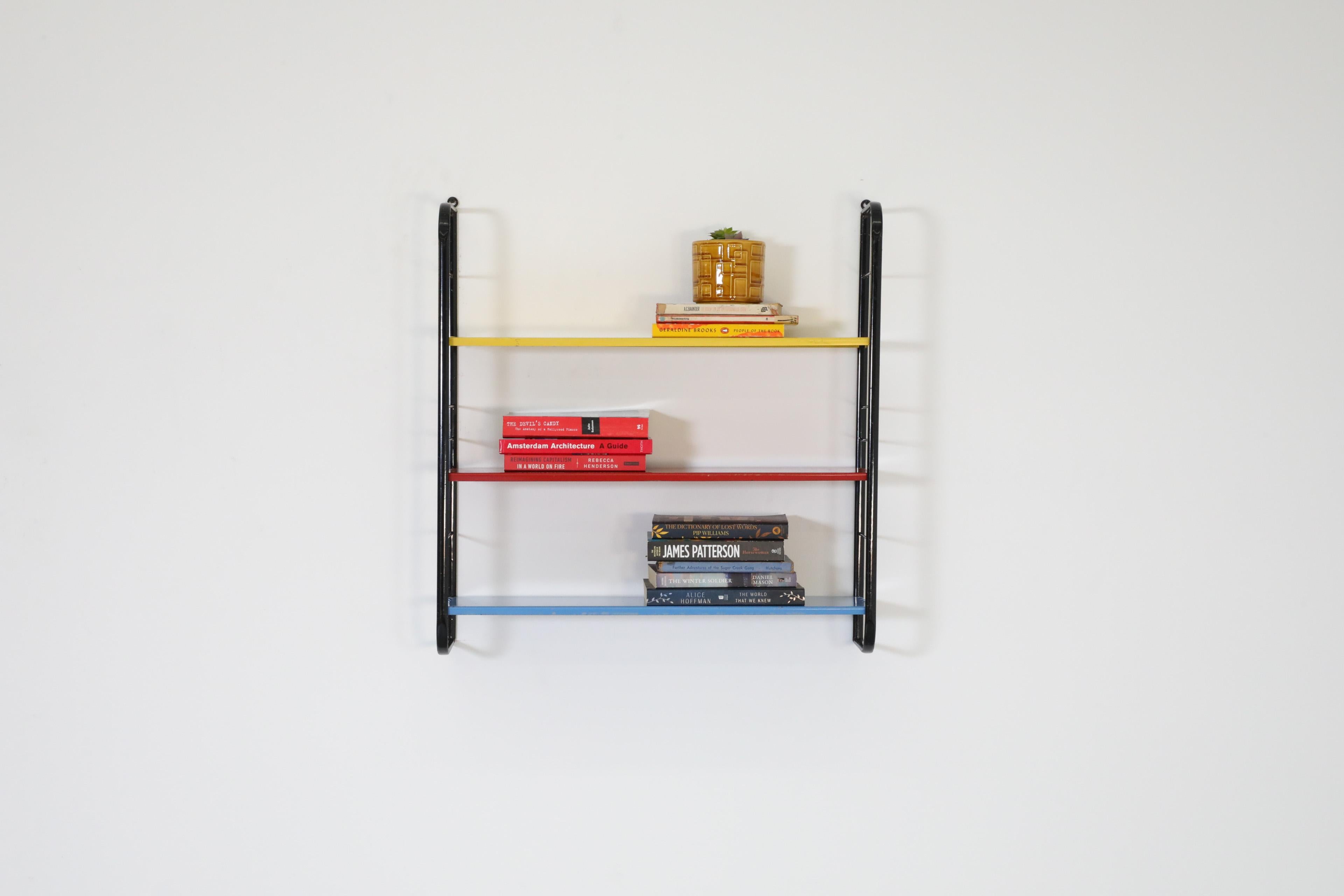 Amazing single section wall mounted shelving unit with adjustable metal enameled shelves on black wire risers. Yellow, red and blue interchangeable industrial style shelves for displaying books and accessories. In original condition with wear