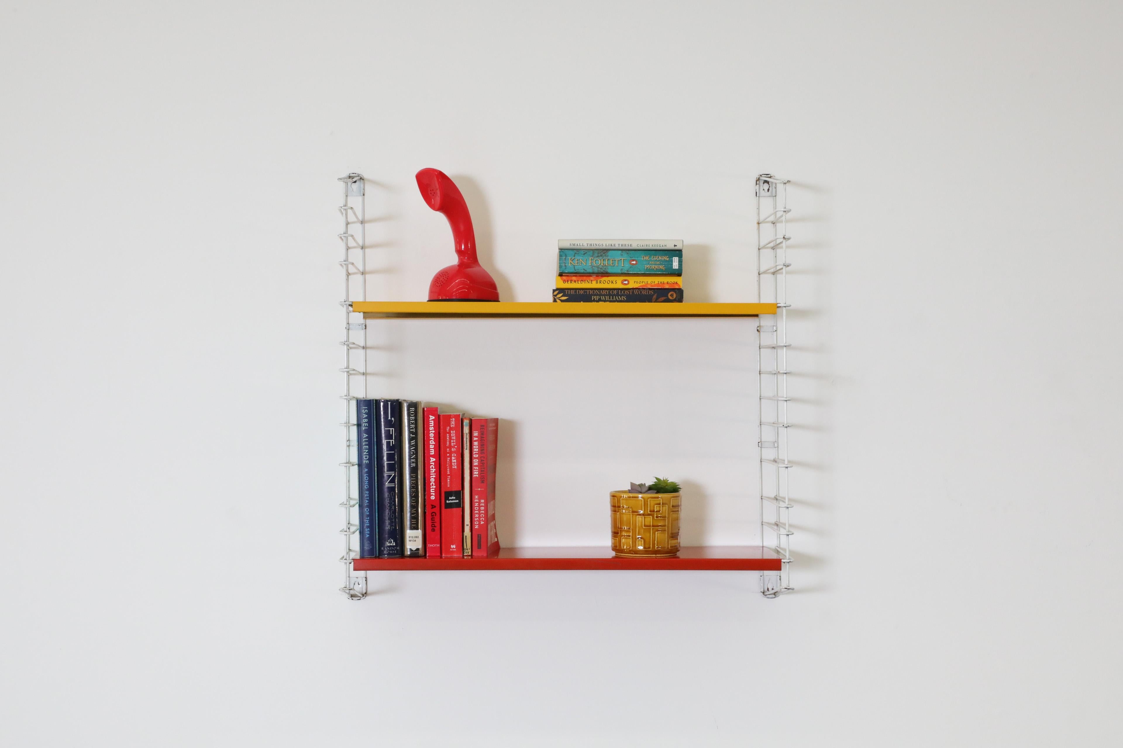 Dutch Mid-Century single section Tomado wall mounted shelving unit by Jan Van Der Togt. Mustard and red enameled metal shelves on white risers with original manufacture stamp. This stylish wall mount shelf is a chic and functional addition to any