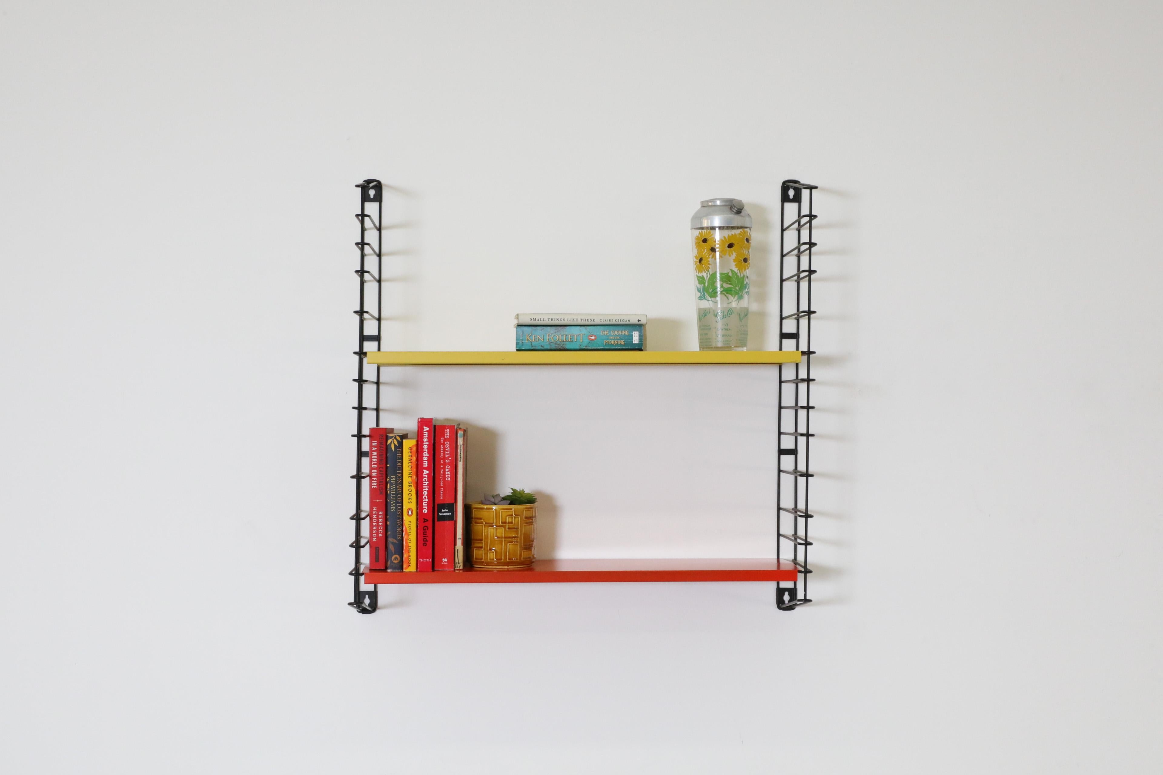 Single section of original Tomado wall mounted shelving unit with yellow and orange metal shelves on black wire risers. Attractive industrial style book or display shelf. In original condition with visible wear consistent with its age and use. Ships