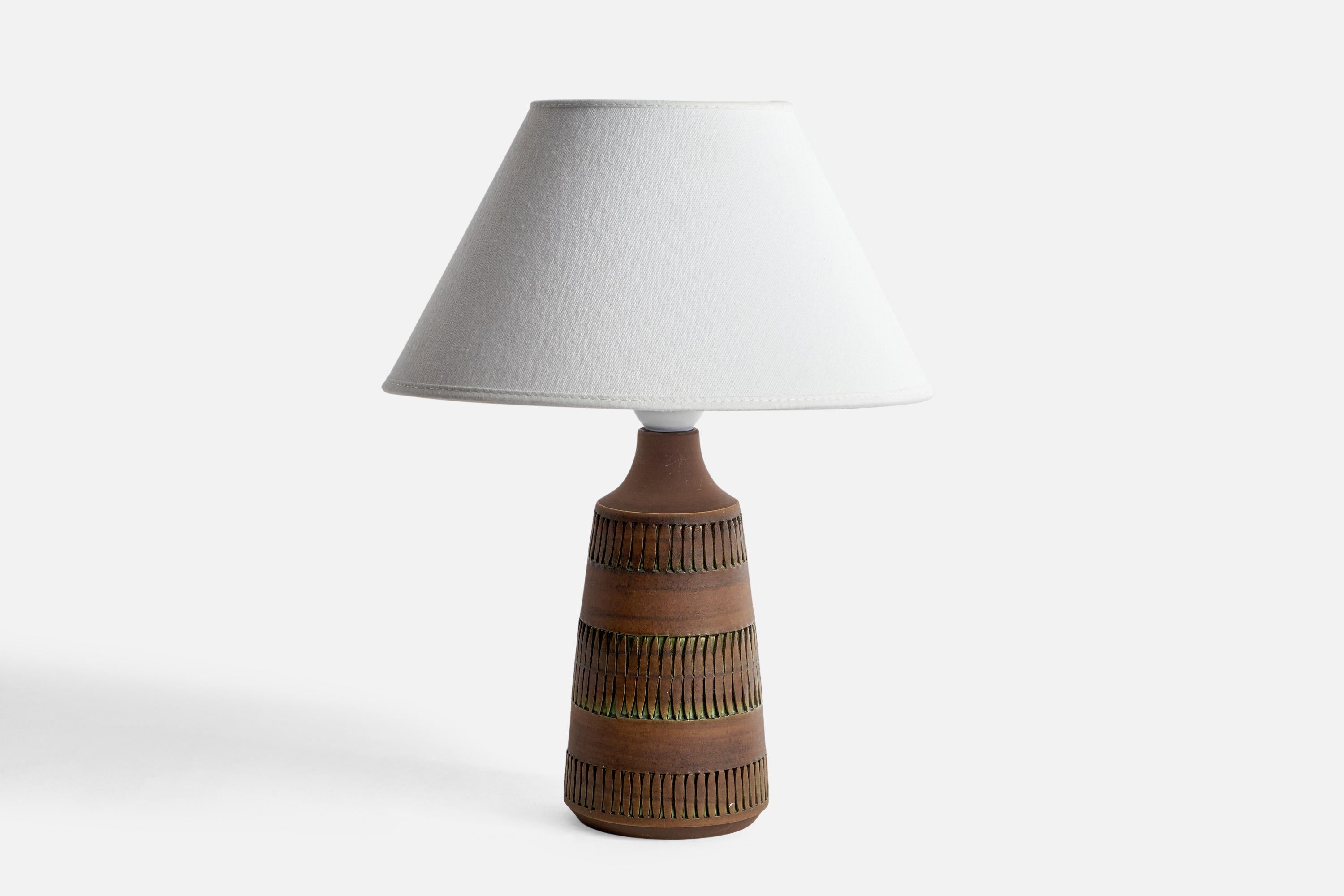 A brown-glazed incised table lamp designed and produced by Tomas Angarius, Sweden, c. 1960s.

Dimensions of Lamp (inches): 9.5” H x 3.8” Diameter
Dimensions of Shade (inches): 4.5” Top Diameter x 10” Bottom Diameter x 5.25” H
Dimensions of Lamp with