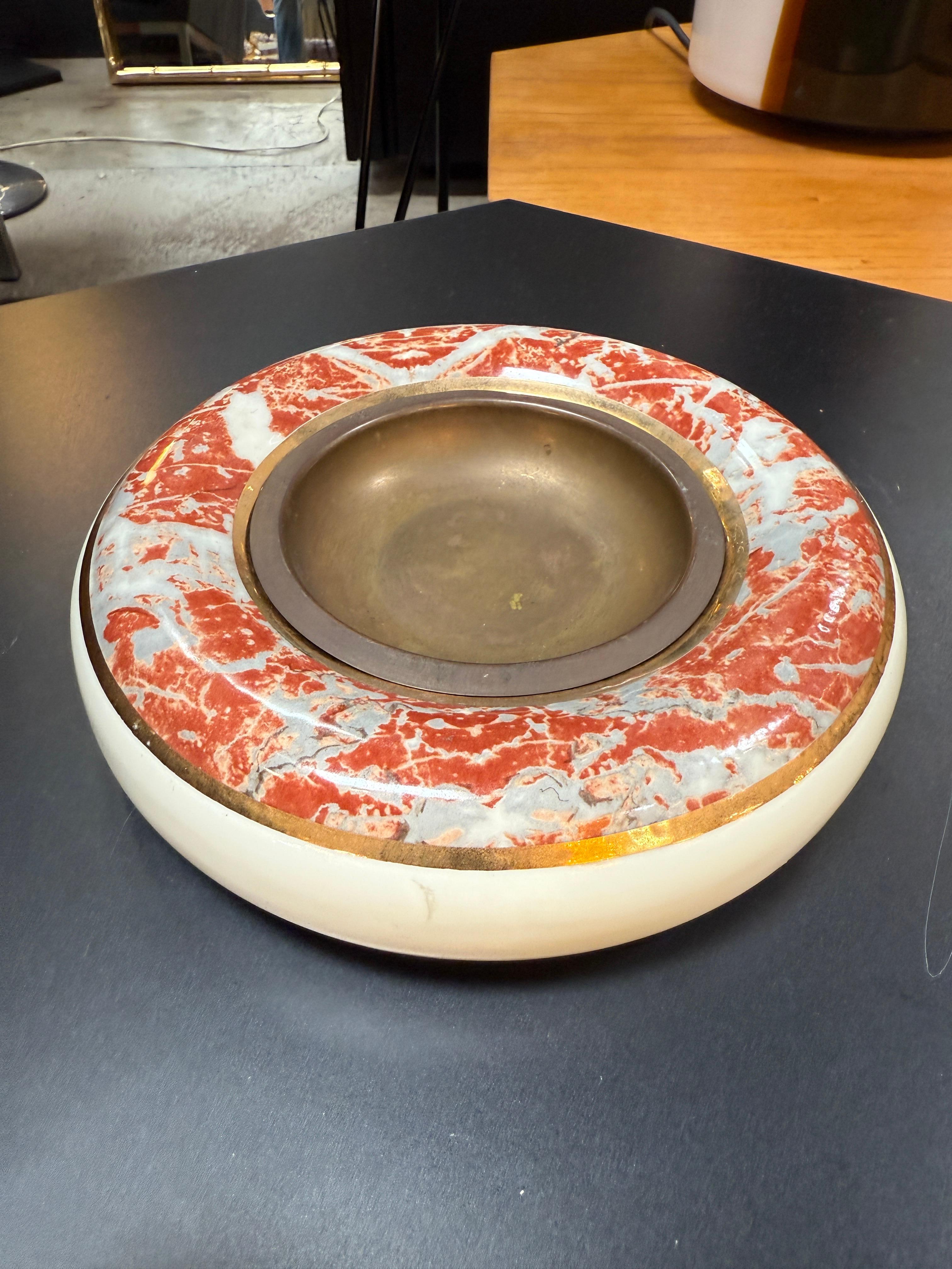 Este llamativo cuenco para centro de mesa de Tomaso Barbi ejemplifica el refinado enfoque del diseñador italiano hacia las artes decorativas de mediados del siglo XX. Realizada en cerámica con una inserción de latón, la pieza presenta una forma