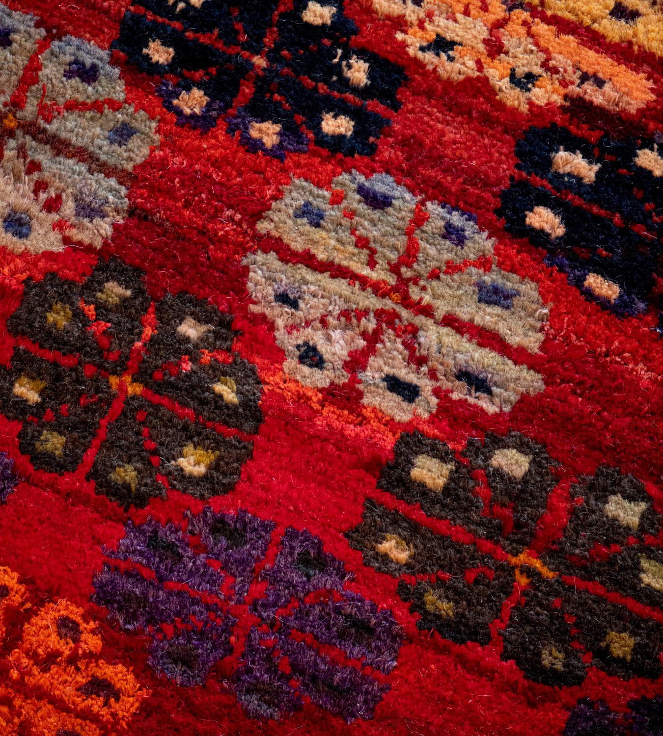 This vintage handwoven wool Turkish rug has a shaded tomato-red field with horizontal bands of polychrome stylized floral lozenges.