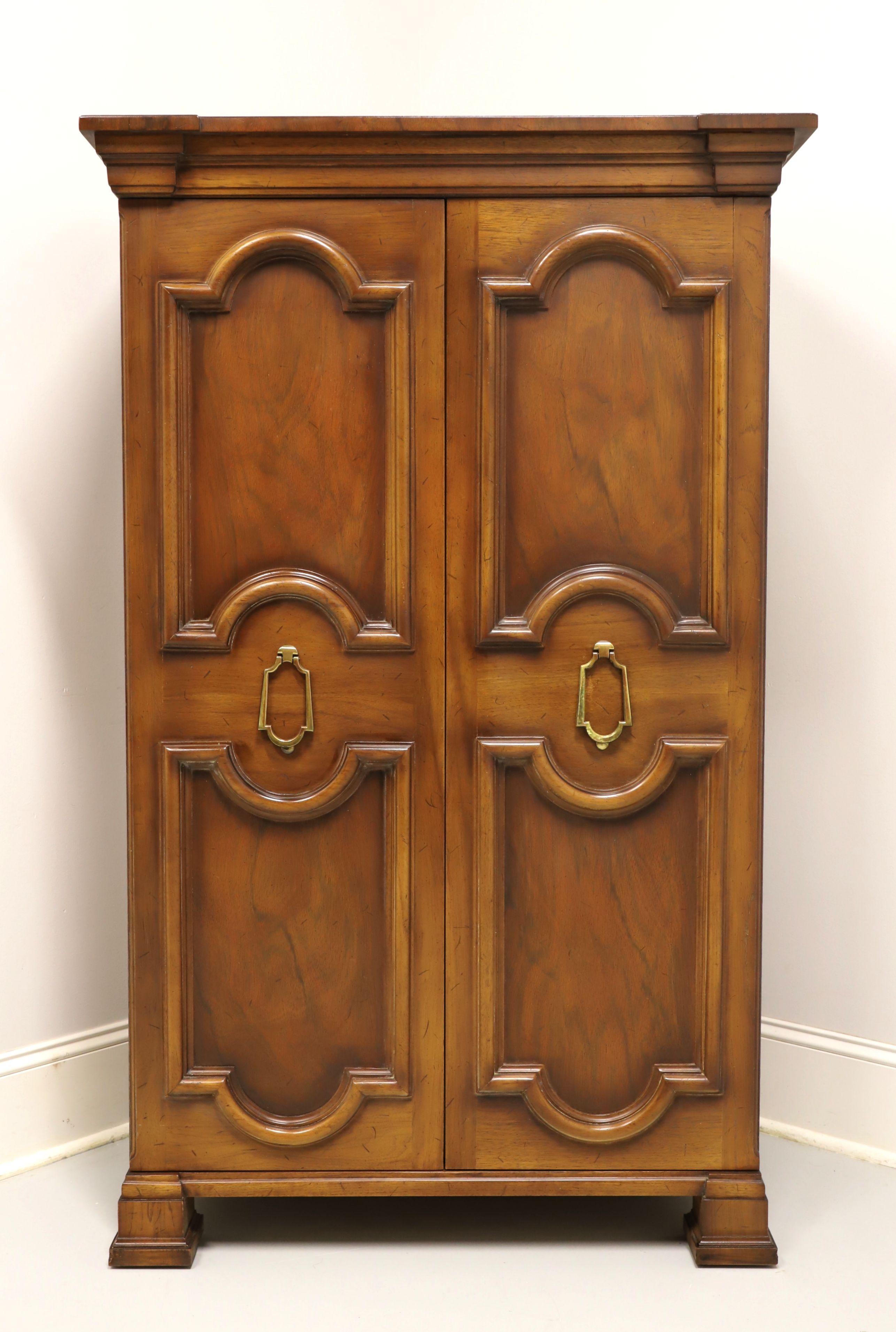 A Hollywood Regency style gentleman's chest by Tomlinson Furniture. Walnut with their slightly distressed Nutmeg finish, raised panel doors, brass hardware and block feet. Features decoratively carved double doors revealing an interior of three