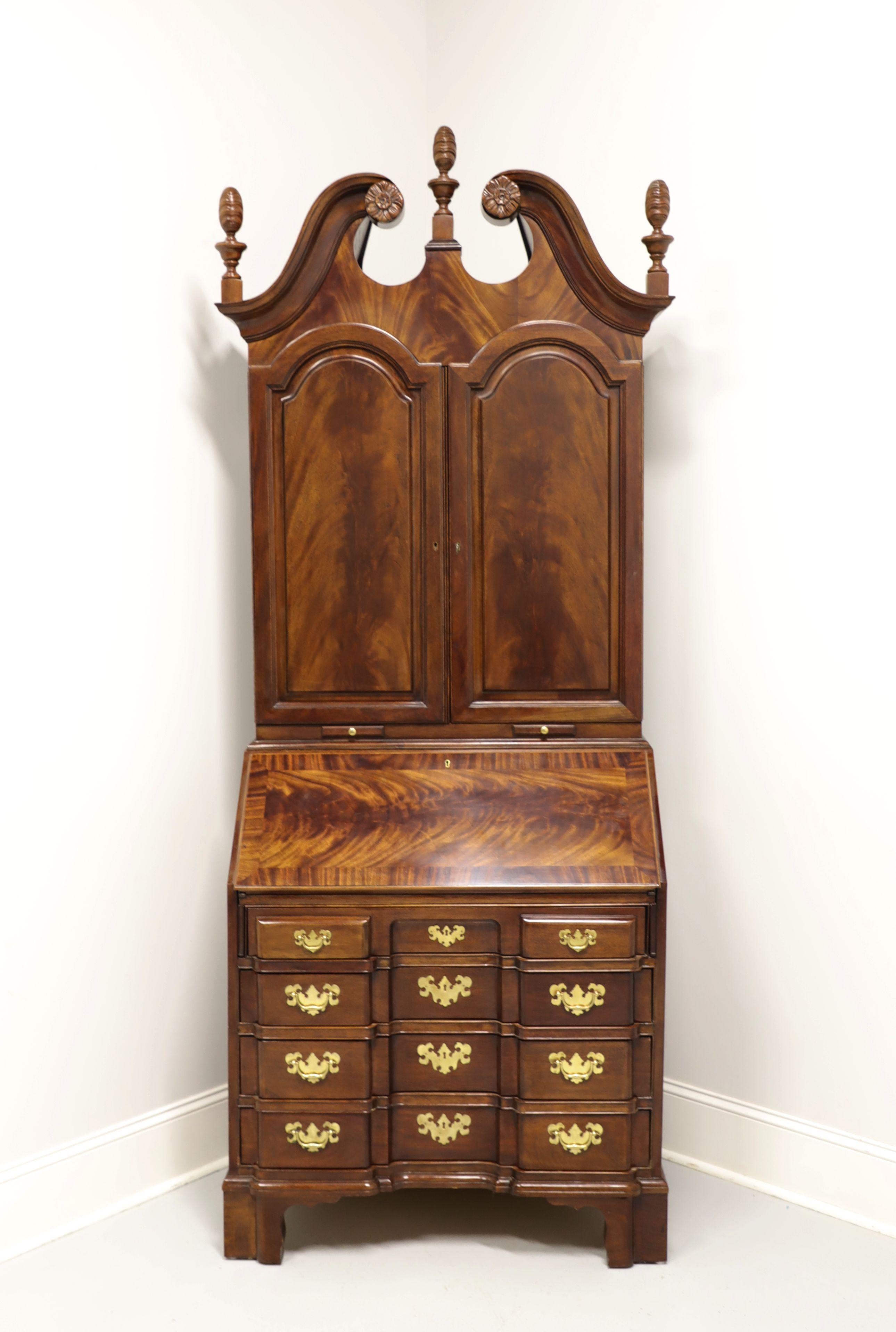 A Chippendale style secretary desk by Tomlinson. Crotch mahogany with brass hardware, pediment top with three finials and bracket feet. Upper blind bookcase has two lockable doors that reveal two adjustable wood shelves and two pull out candle