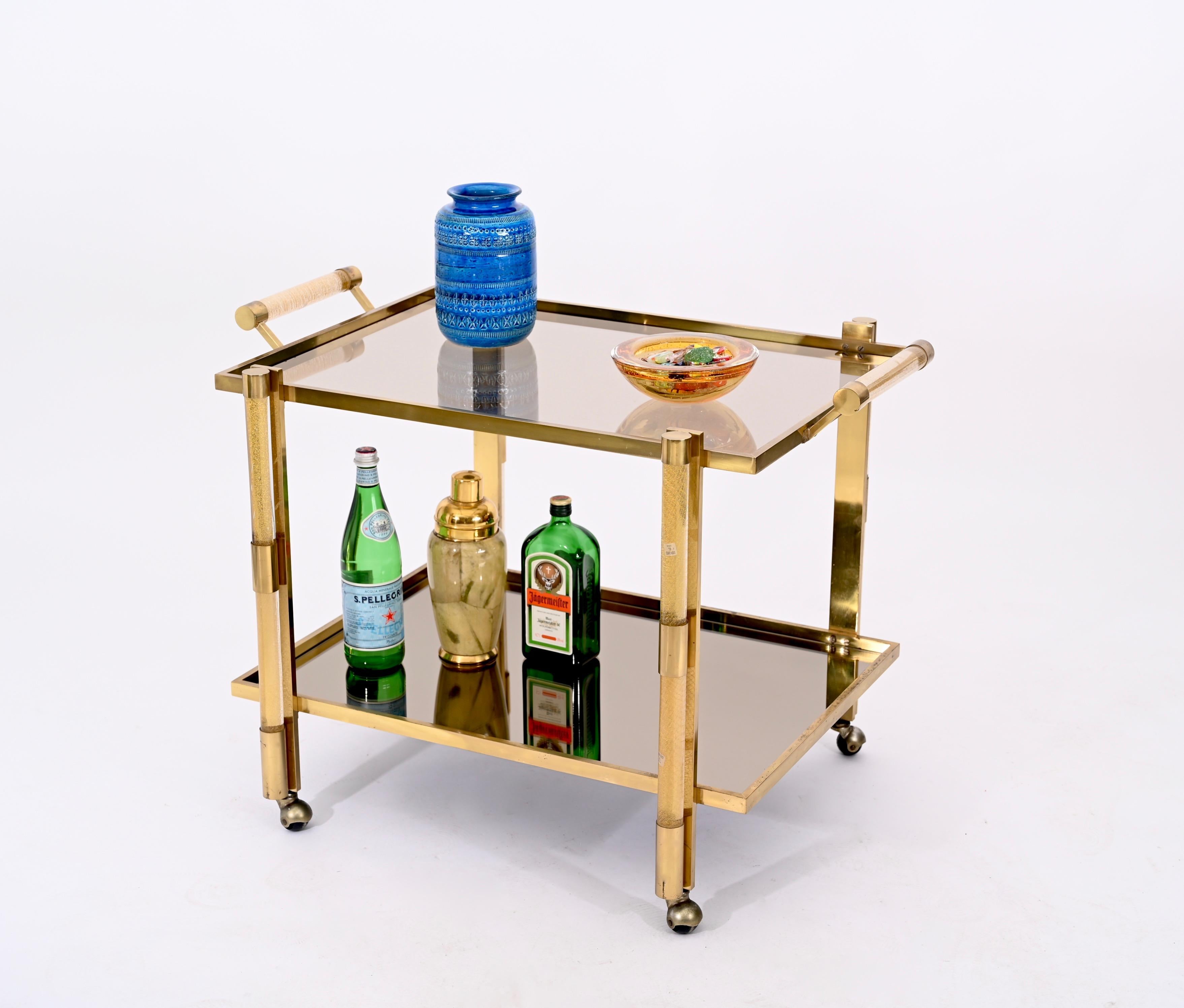 Fantastic bar trolley in brass, Murano glass with gold inside. This luxurious bar cart is an incredibly rare piece that was designed by Tommaso Barbi and produced by Murano Vetri D'arte in Italy in the 1970s.

The structure of the cart is made in
