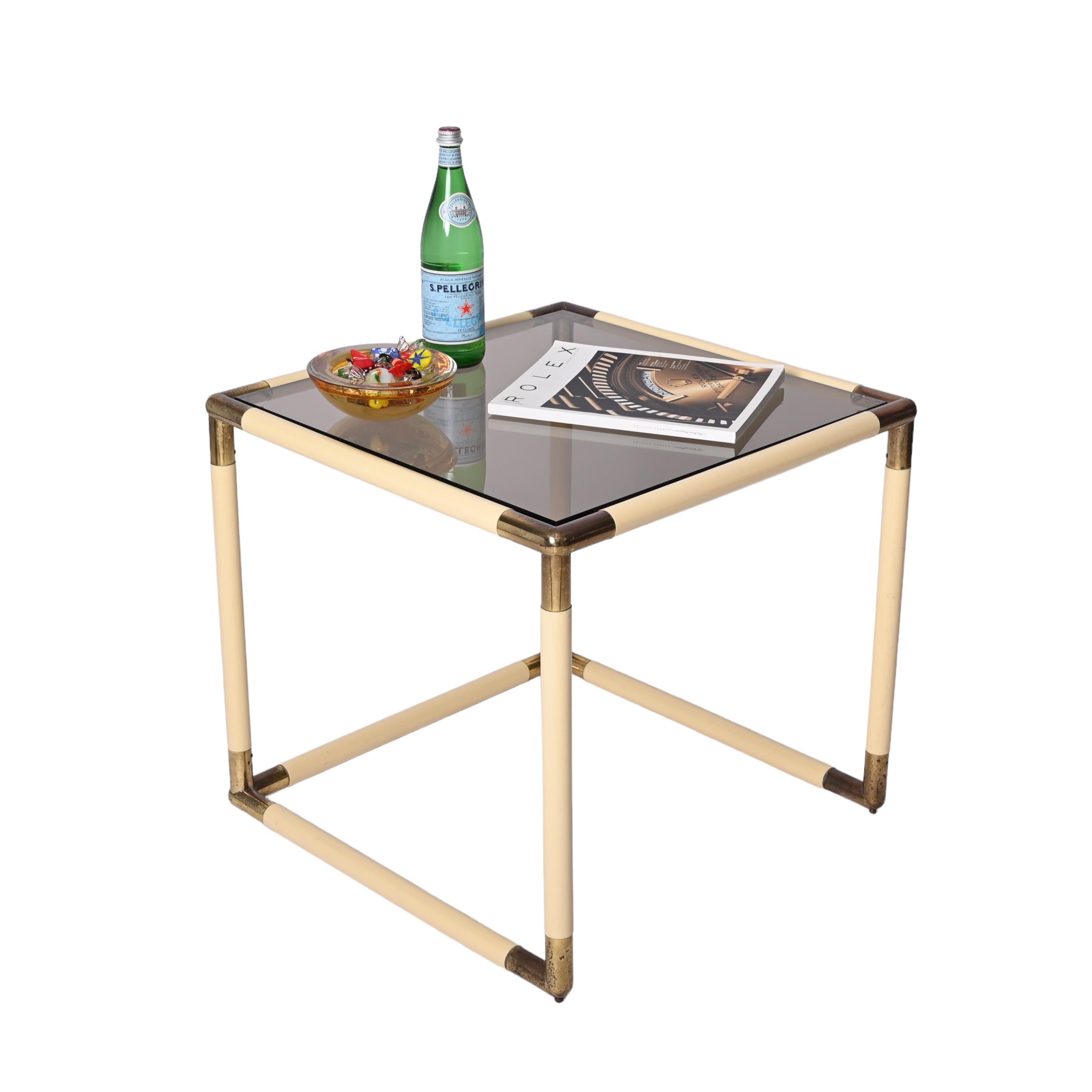 Midcentury cube shaped coffee table designed by Tommaso Barbi and produced in Italy in the 1970s.

The coffee table is made in a lovely cream enamelled metal, with brass angles and smoked glass top. The patina on the brass corners make it even