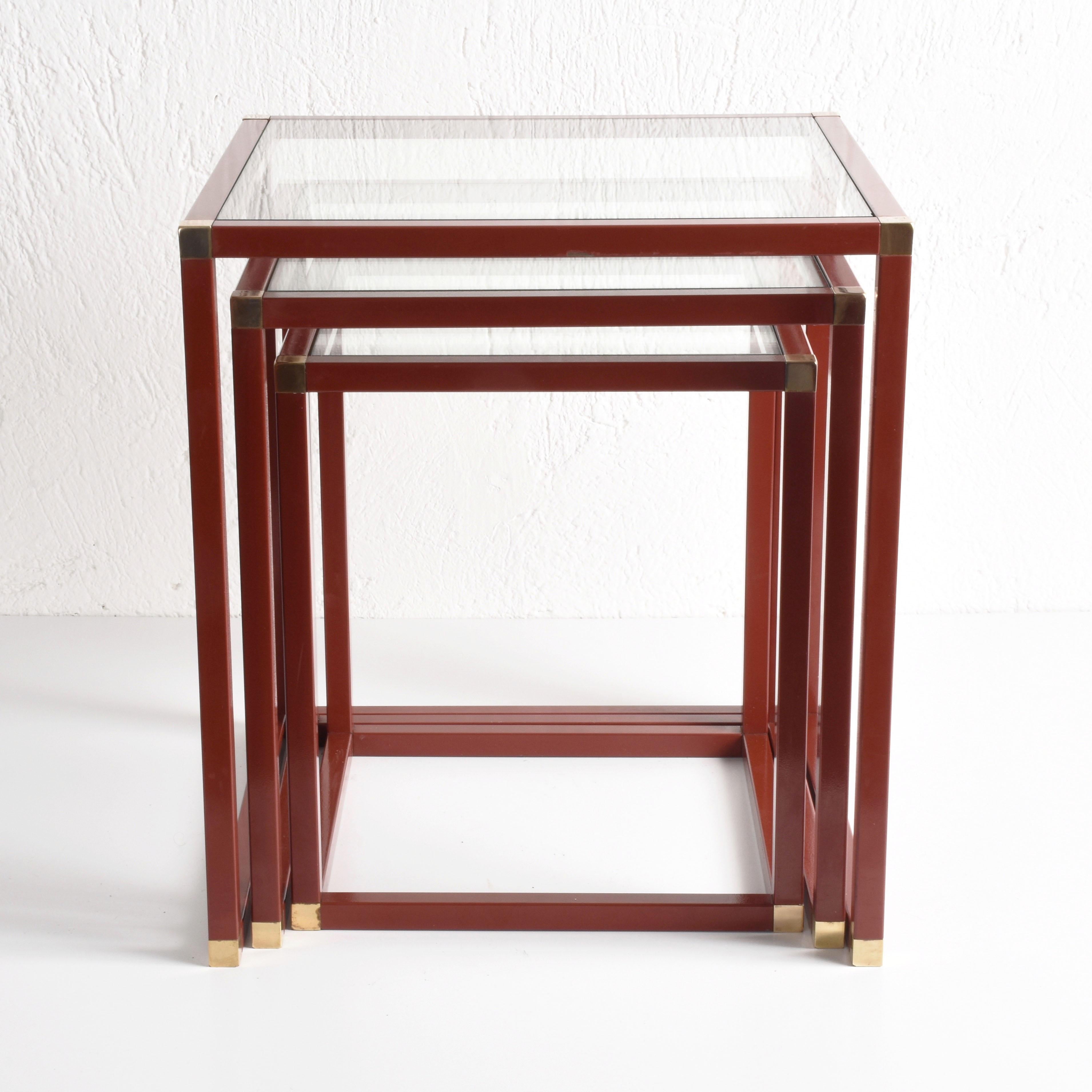 Midcentury nesting tables in a delicious burgundy red metal, with brass corner pieces and crystal glass. 

Due to their design is highly likely the attribution to Tommaso Barbi as part of an Italian production during the 1970s.

A wonderful set